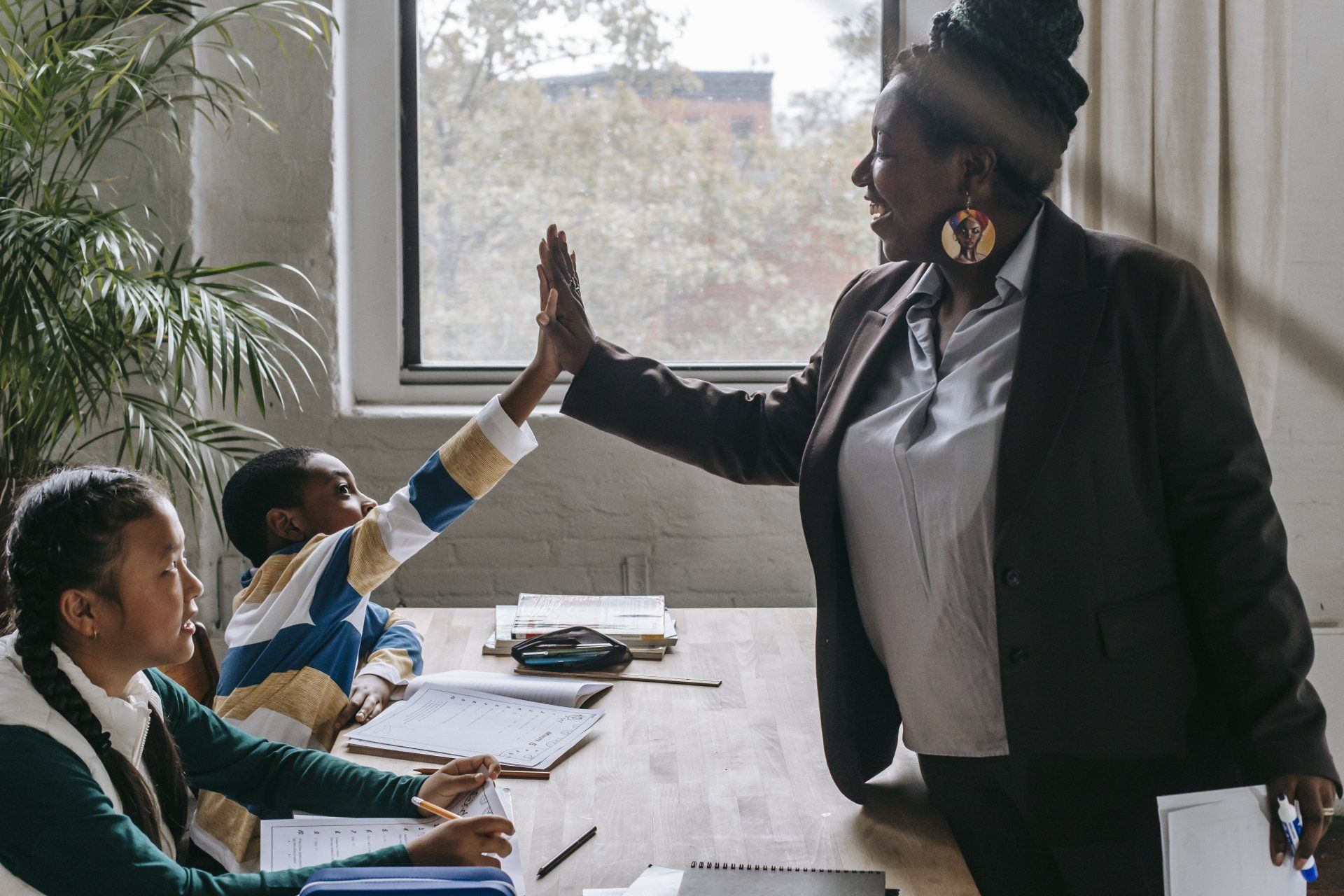 A woman is giving a child a high five in a classroom.