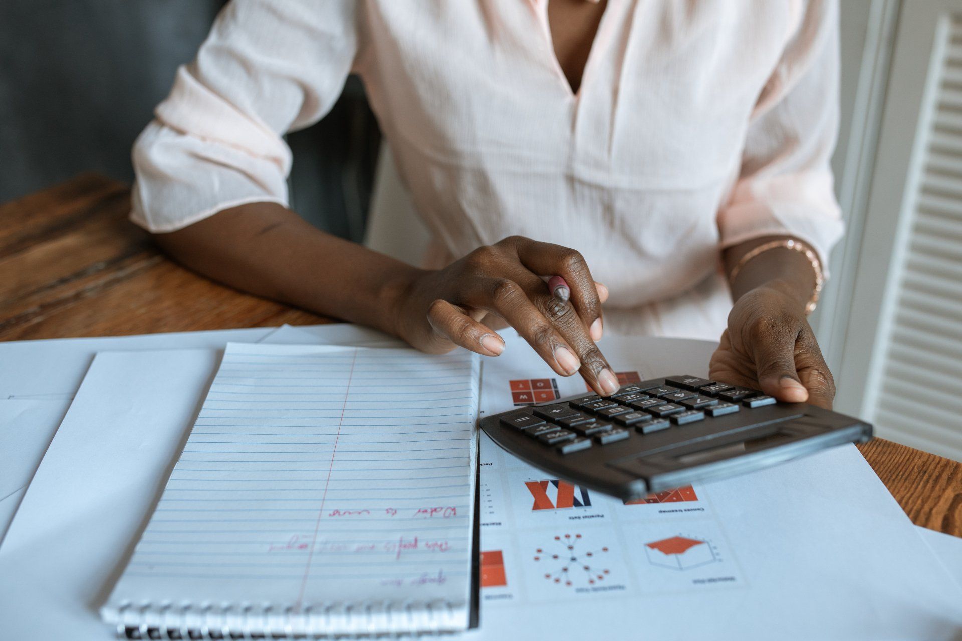 A woman is sitting at a table using a calculator.