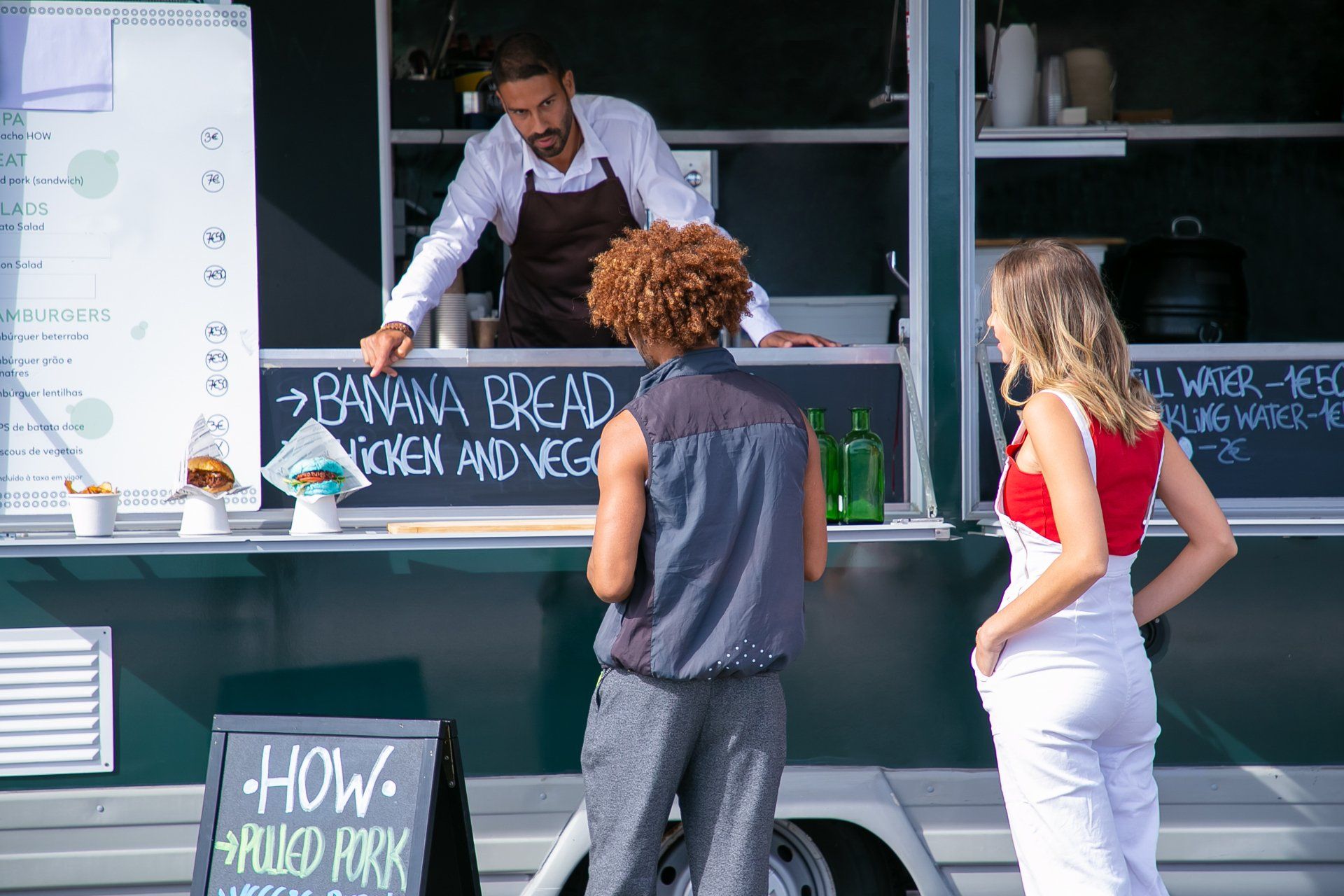 a man is standing in front of a food truck talking to two women .
