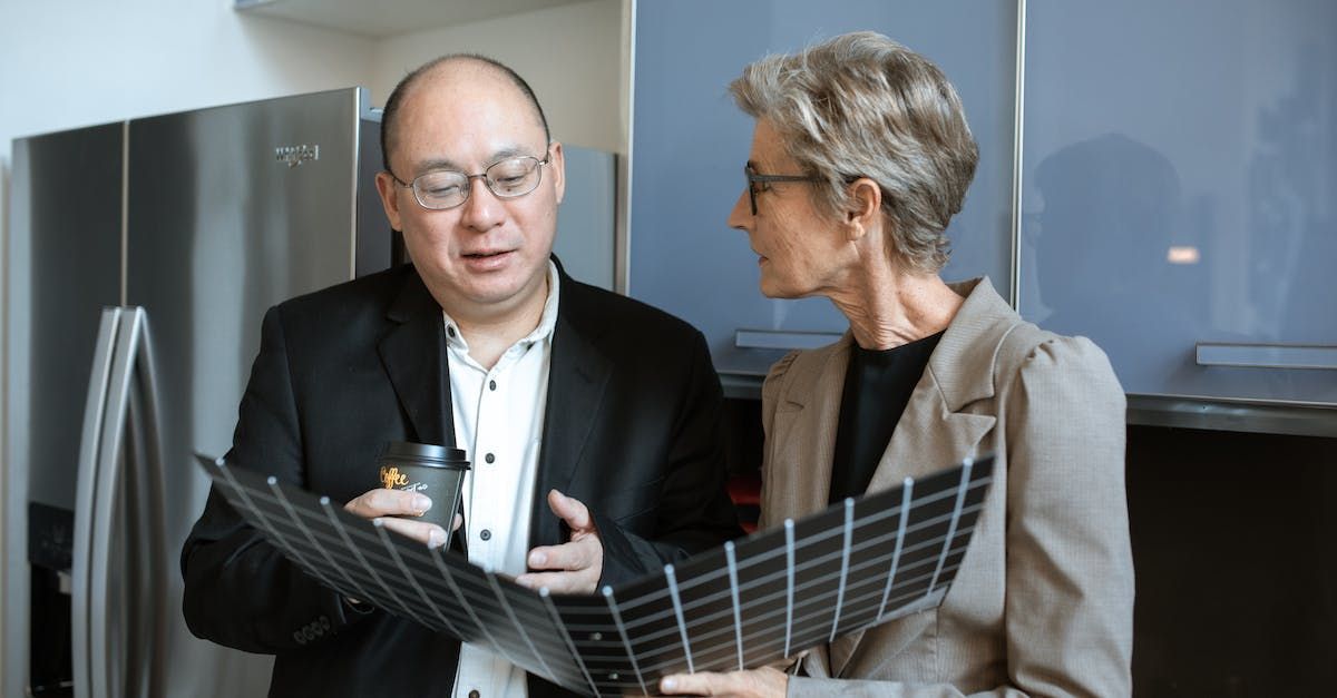 A man and a woman are looking at a piece of paper in a kitchen.