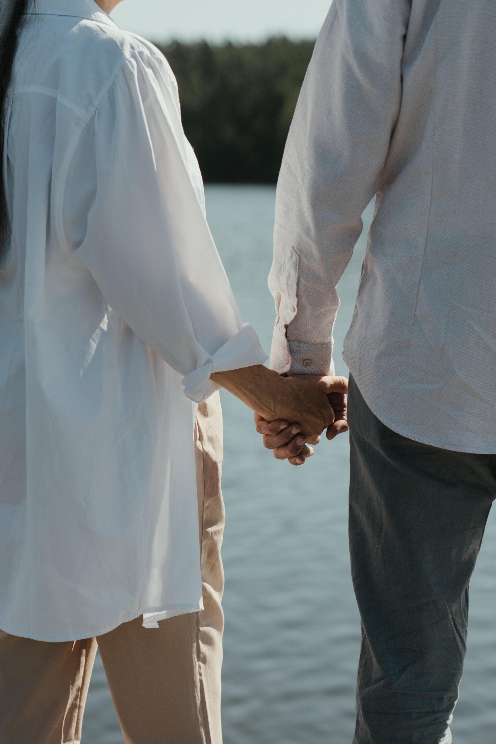 A man and a woman are holding hands while standing next to a body of water.