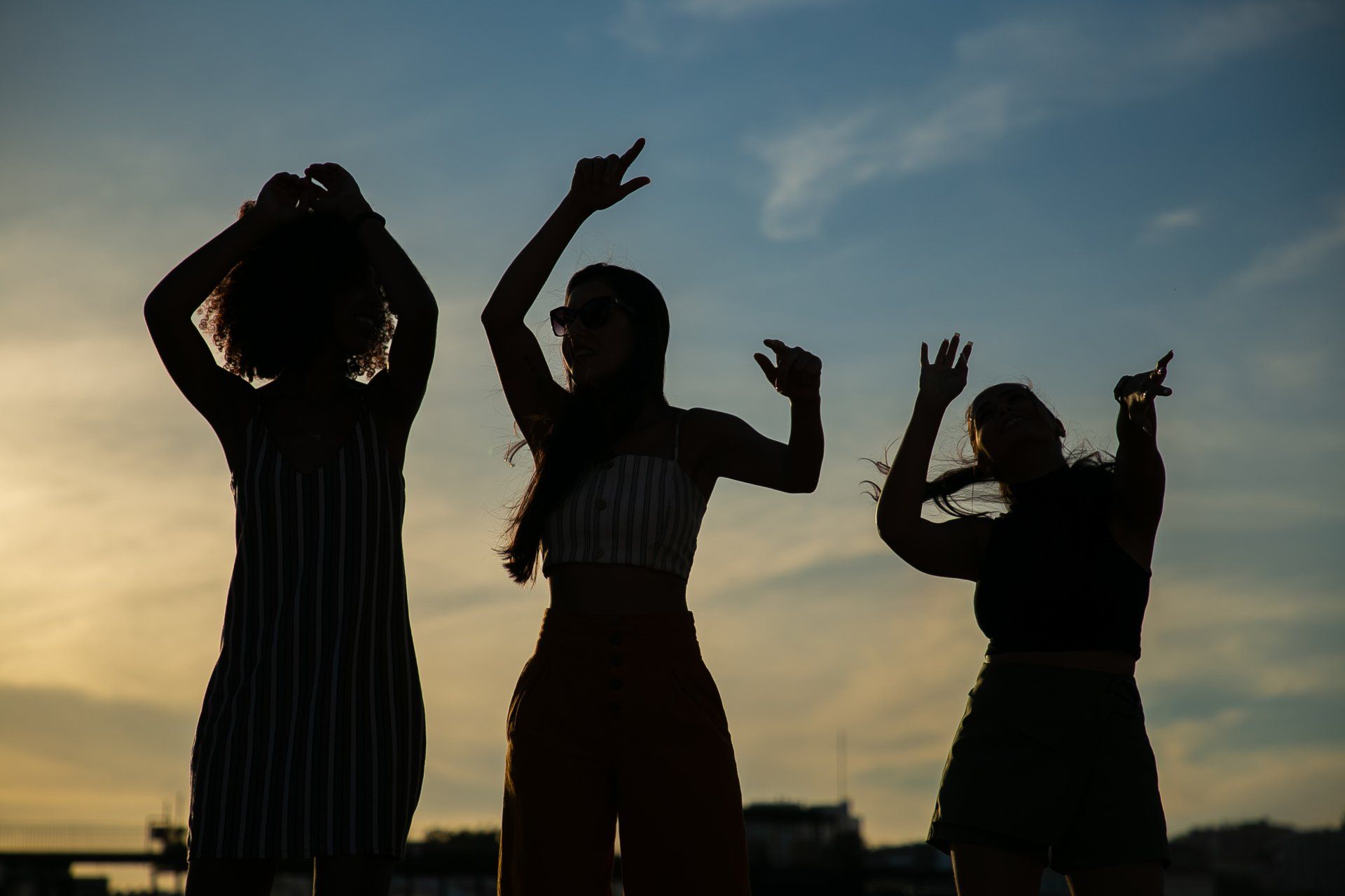 Tre donne sono in piedi una accanto all'altra e ballano al tramonto.