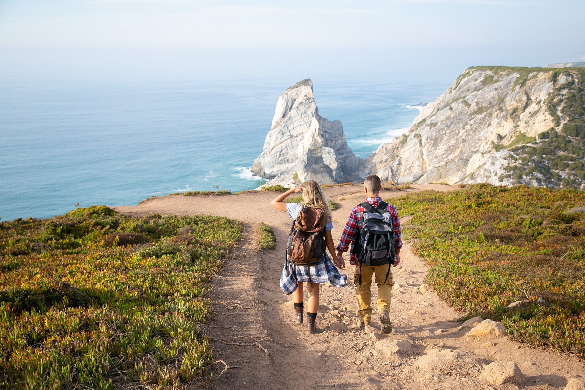 Two hikers walking along a trail with sweeping mountain views