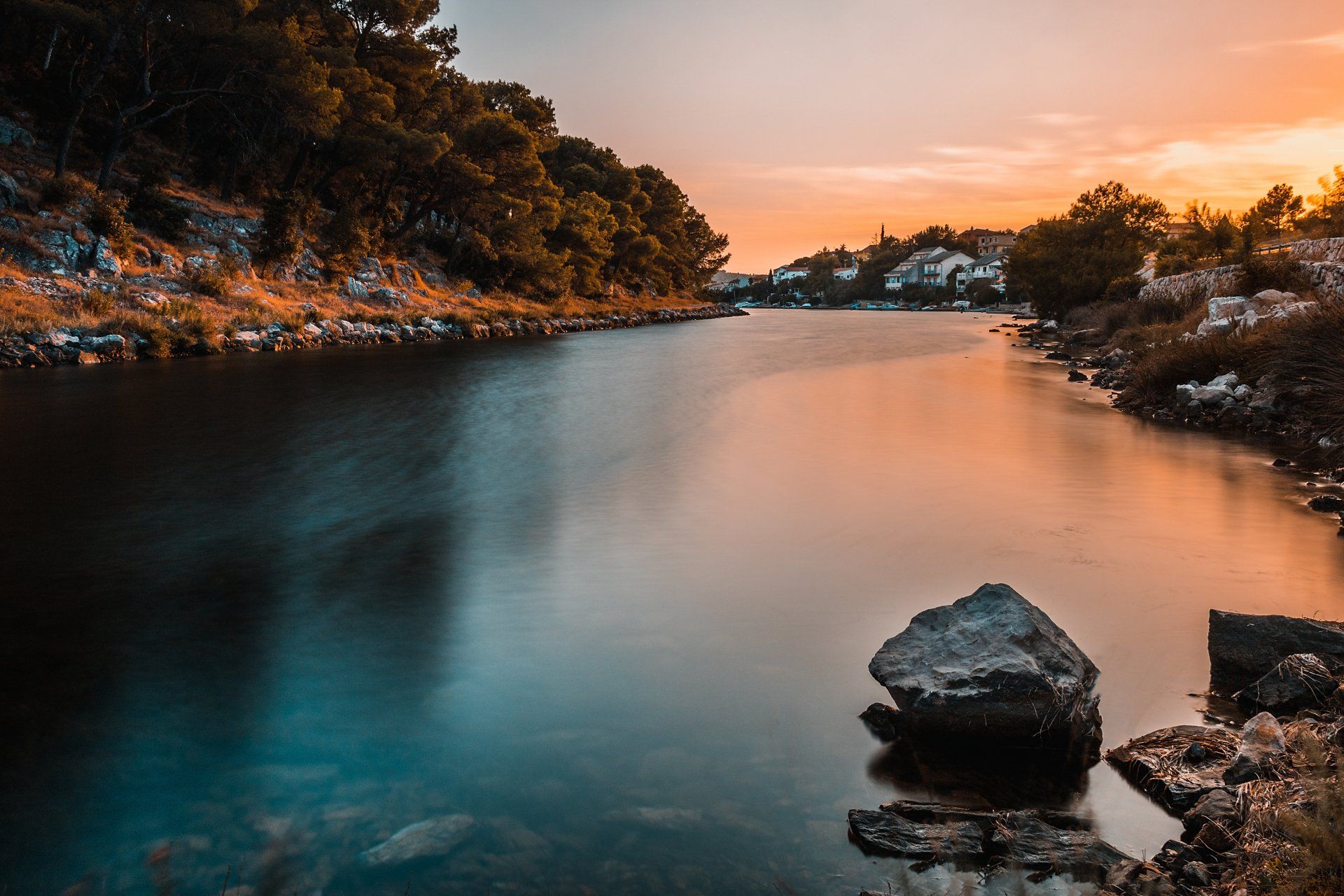 Une rivière entourée d'arbres et de rochers au coucher du soleil.