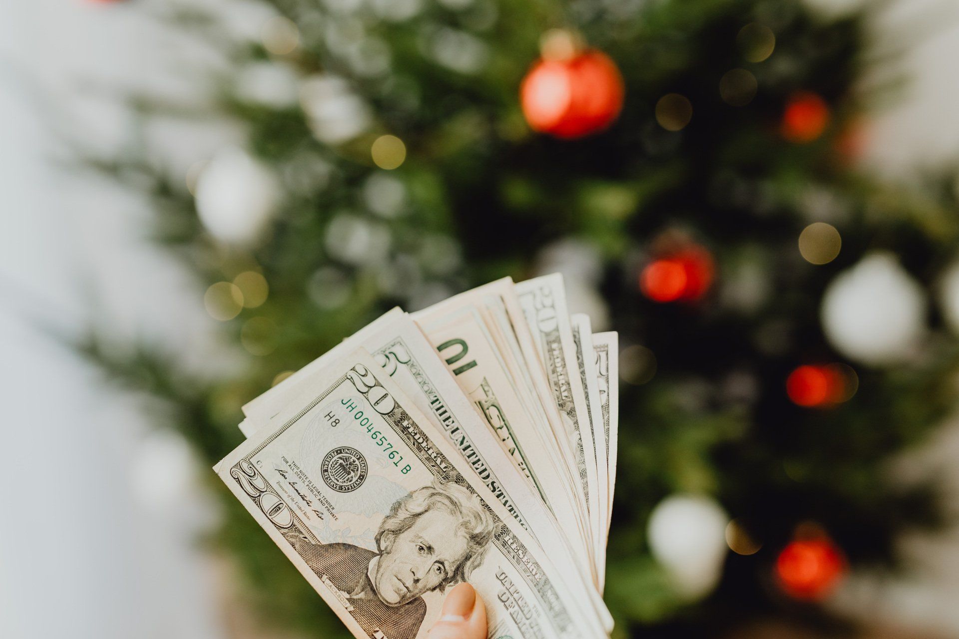 A person is holding a fan of money in front of a christmas tree.