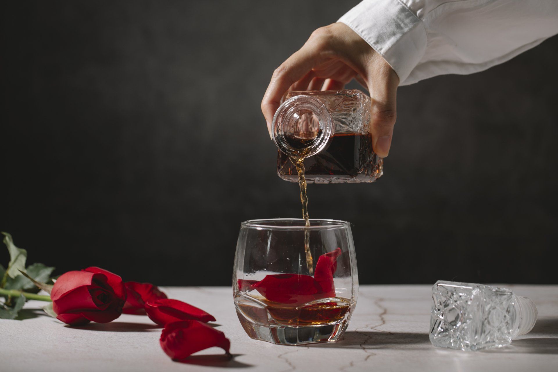 A person is pouring whiskey into a glass with rose petals.