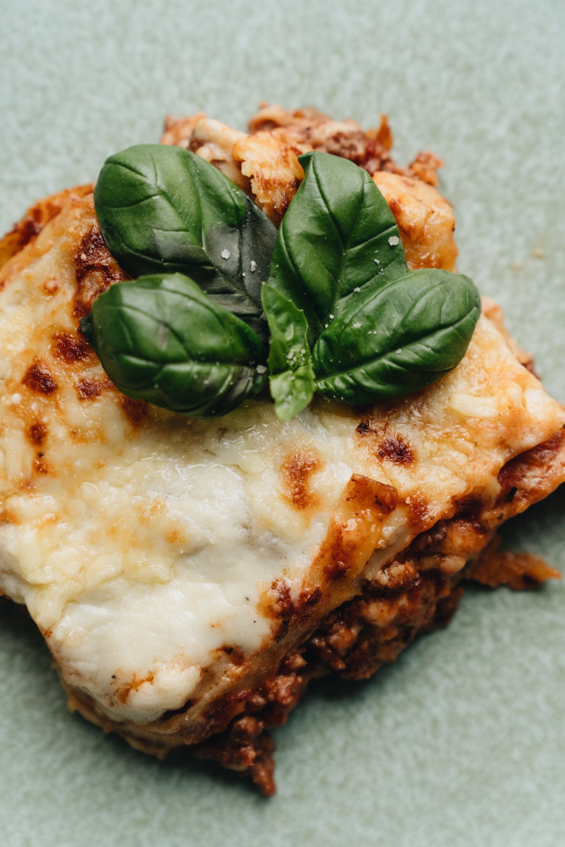 A close up of a lasagna with basil on top on a plate.