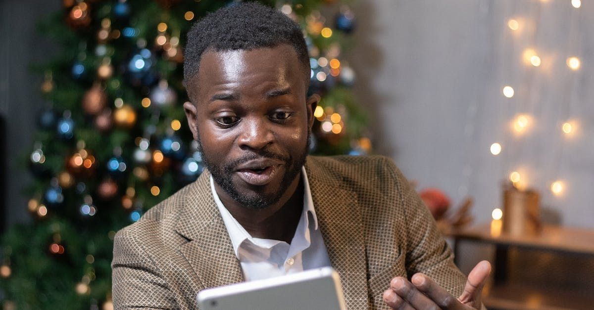 A man is sitting in front of a christmas tree looking at his cell phone.