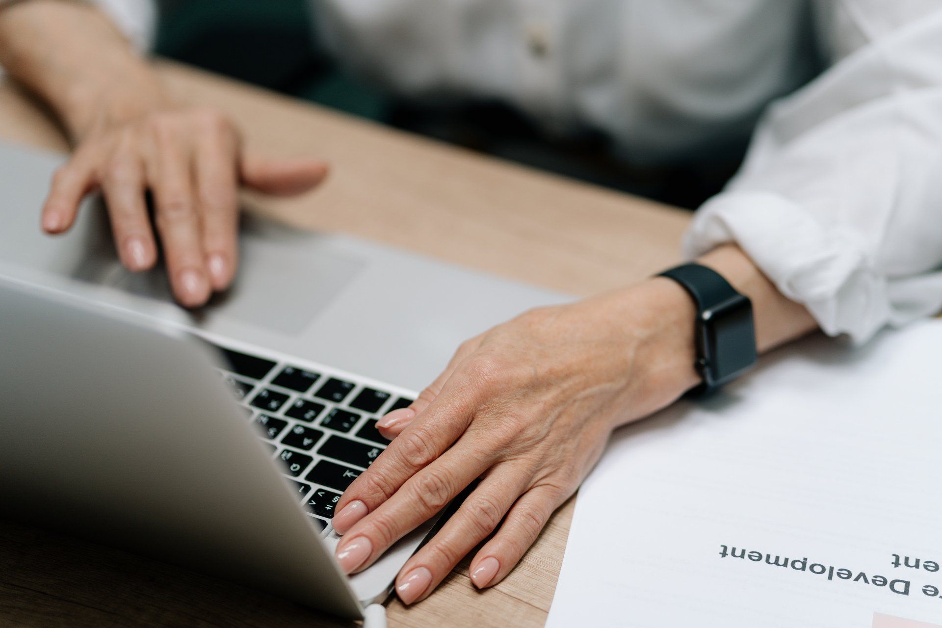 A woman is typing on a laptop computer while wearing a smart watch.