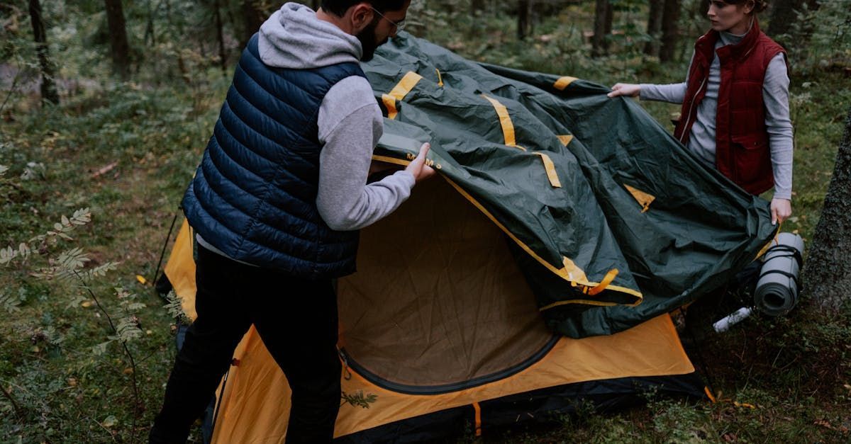 A man and a woman are setting up a tent in the woods.