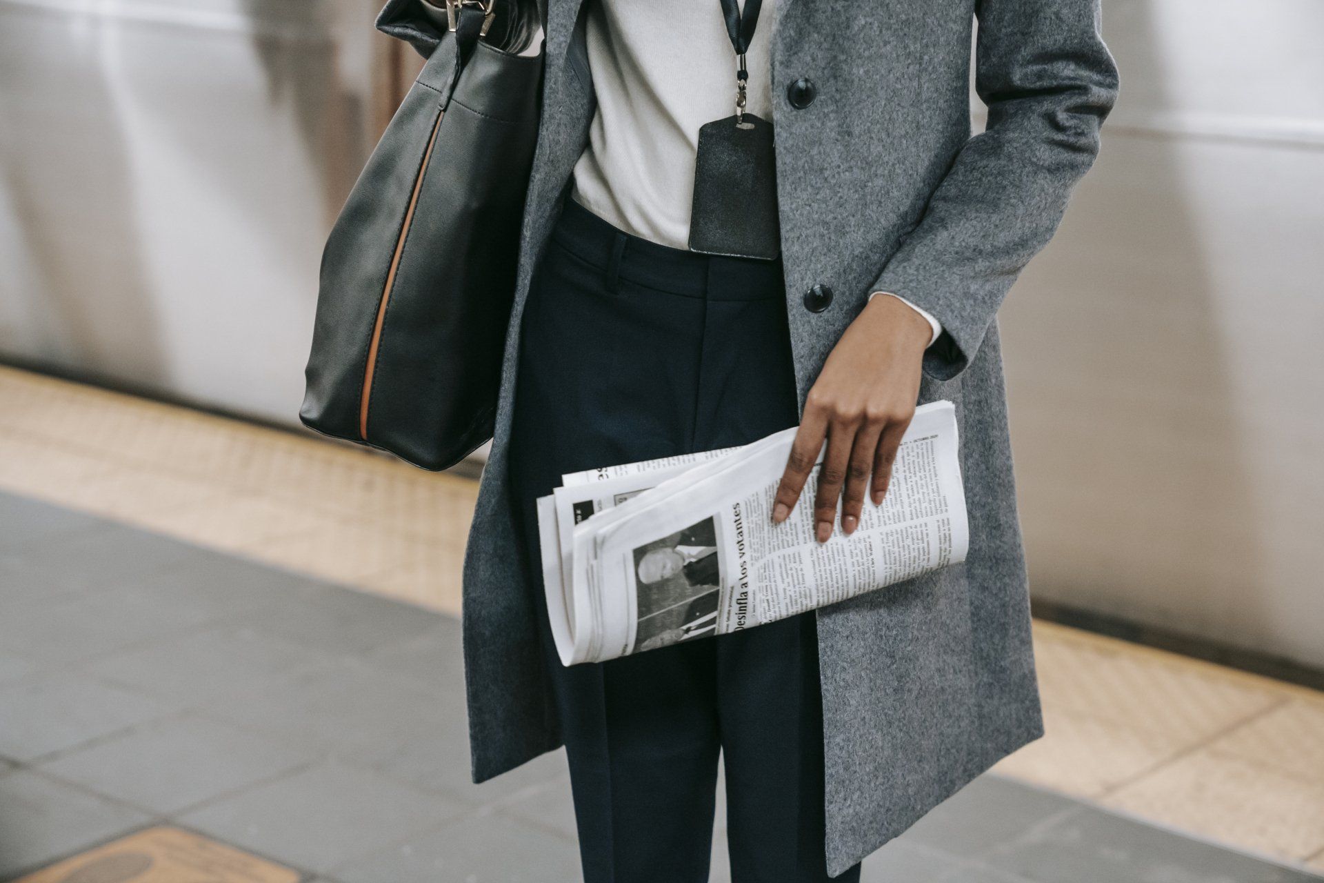 A woman in a coat is holding a newspaper and a bag.