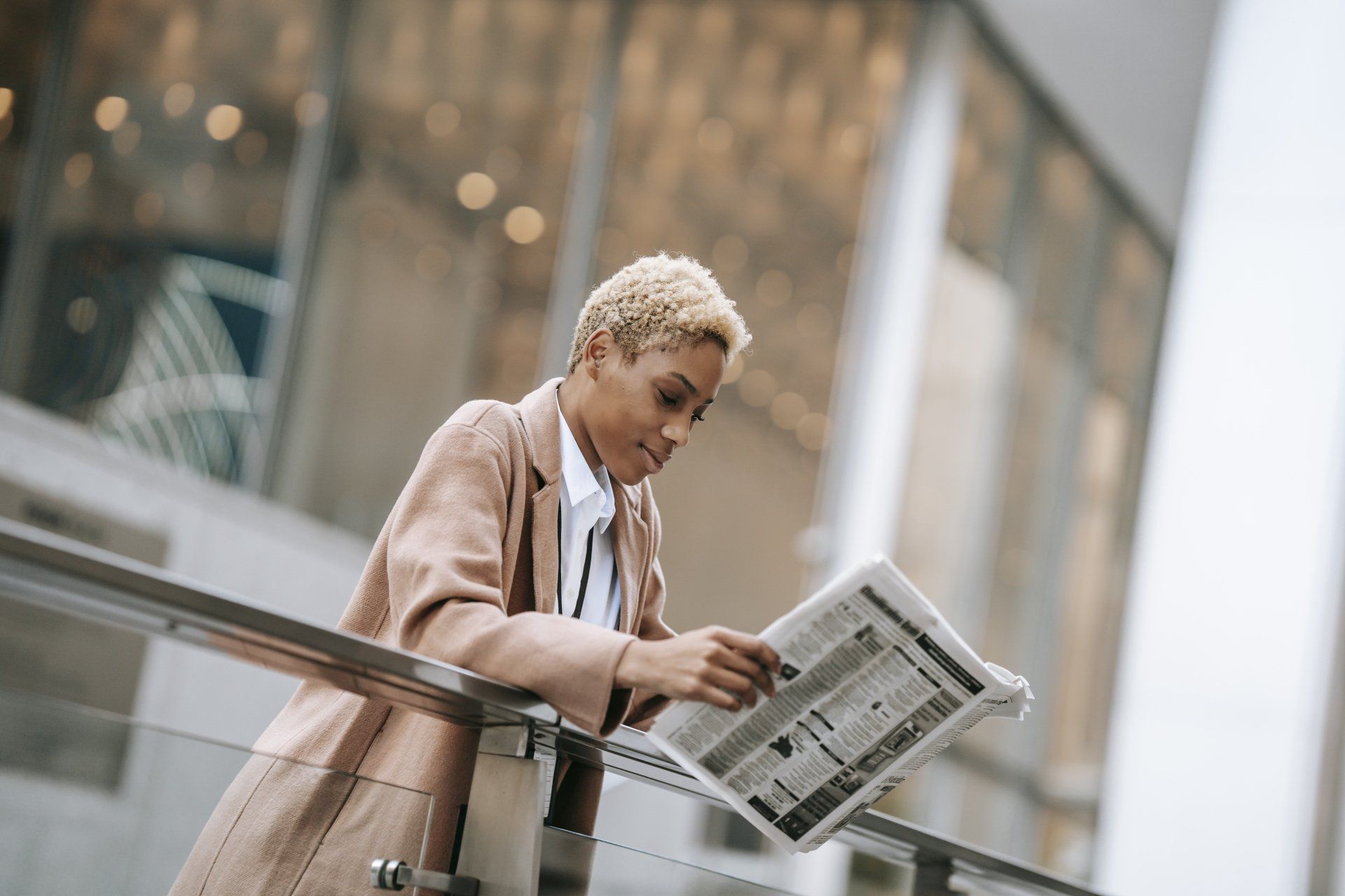 A woman is leaning on a railing reading a newspaper.