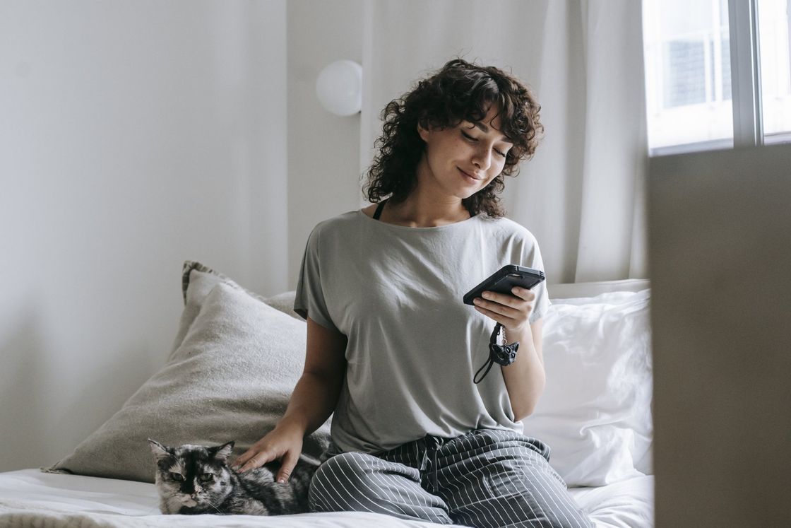 a woman is sitting on a bed with a cat and looking at her phone .