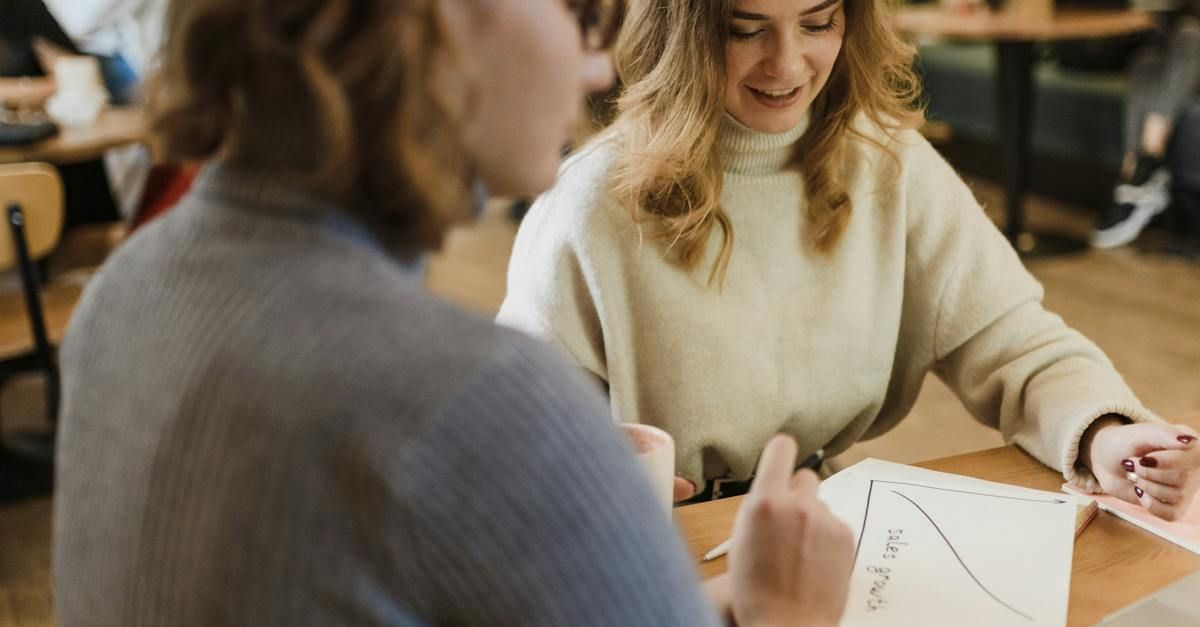 Two women are sitting at a table looking at a graph.