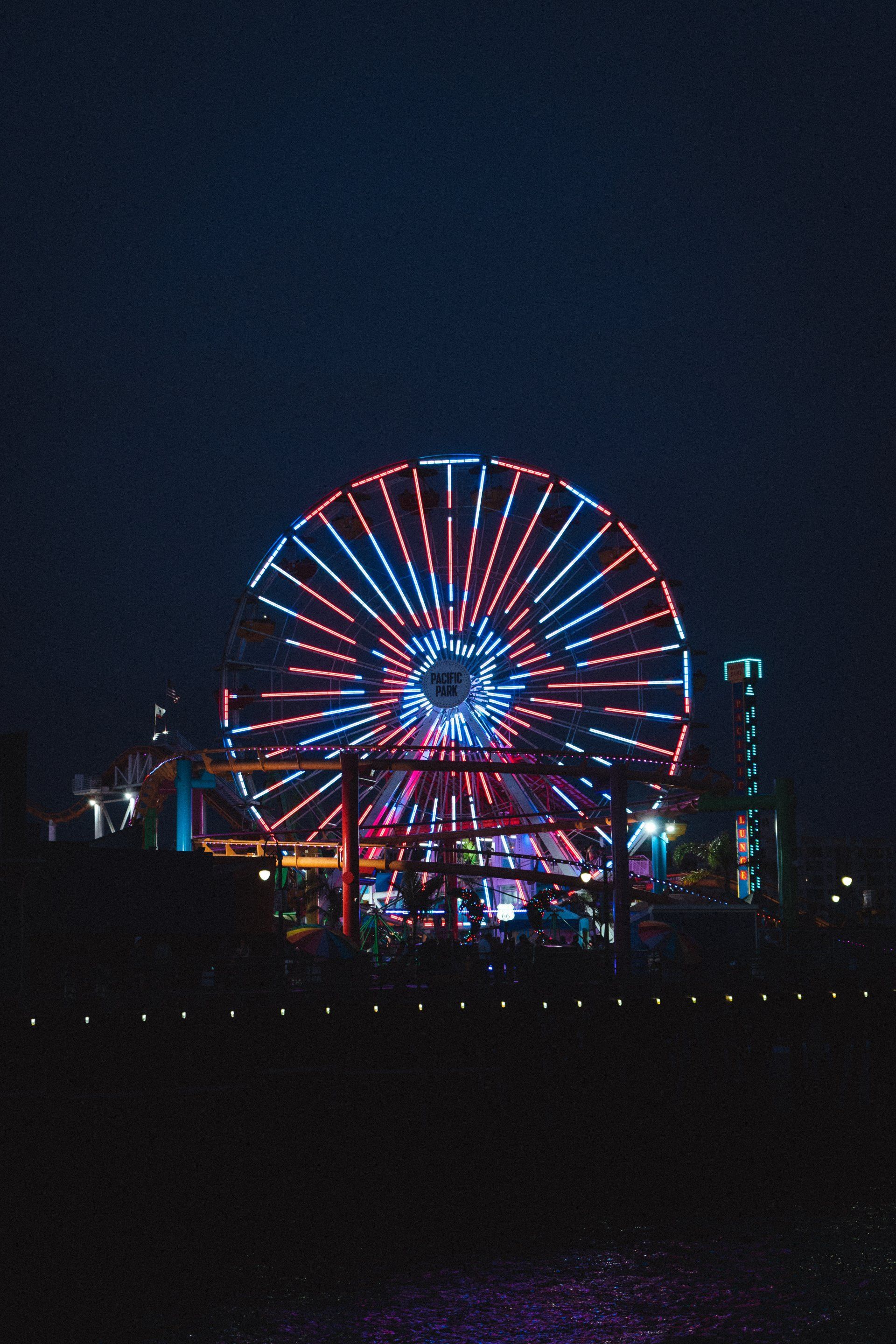 A ferris wheel is lit up at night in an amusement park.