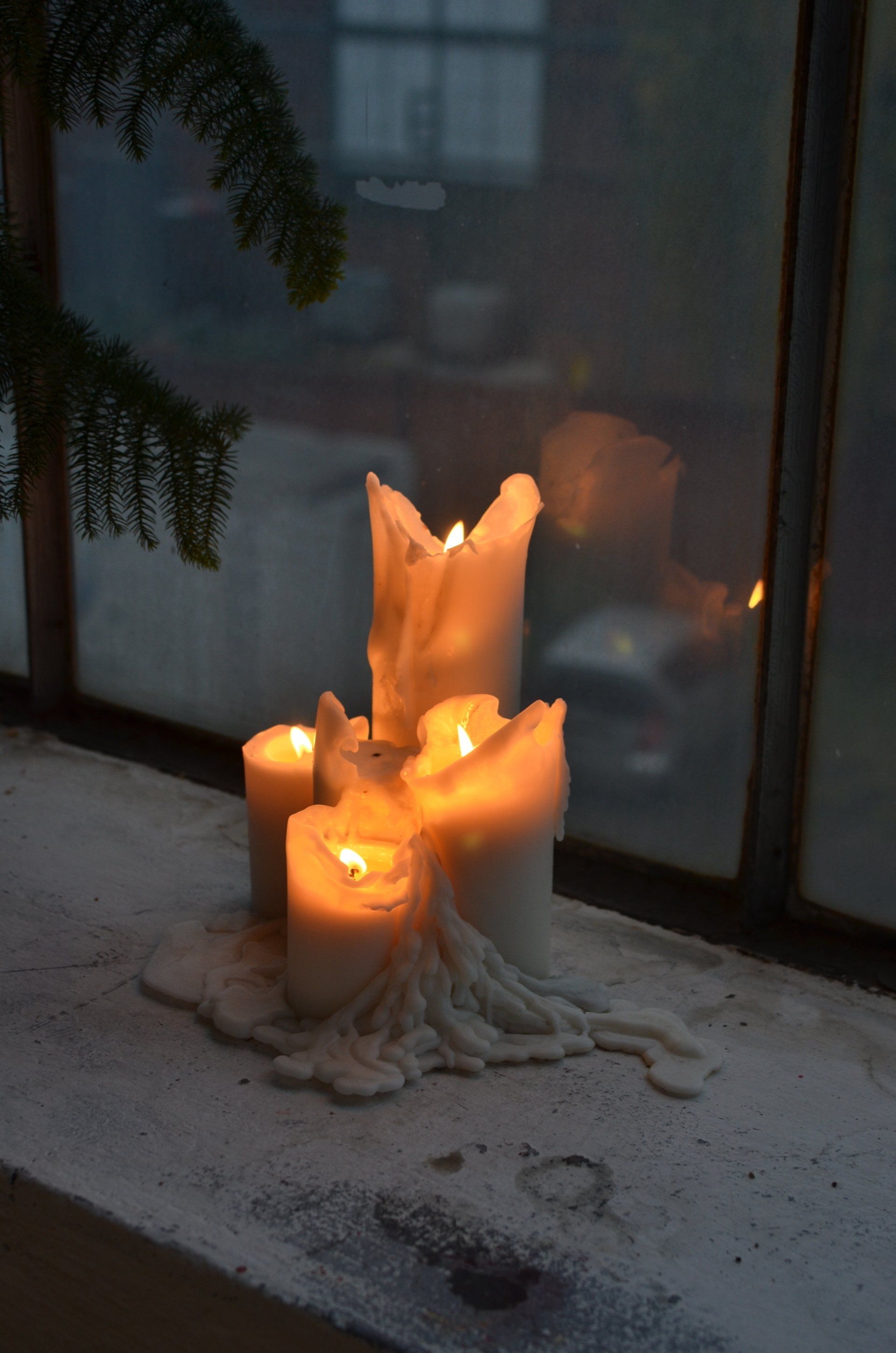 A group of lit candles are sitting on a window sill.