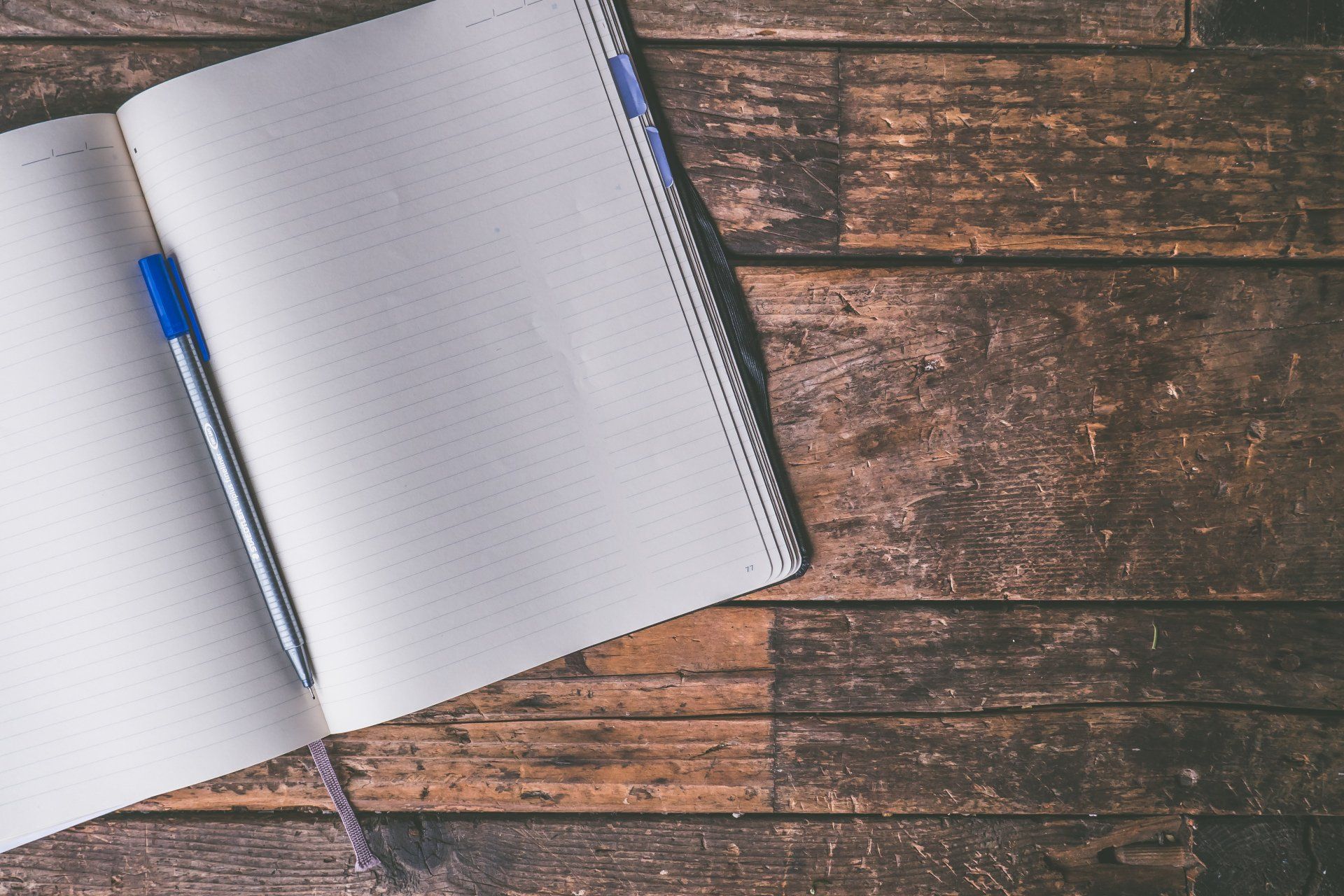 An open notebook with a pen on a wooden table.