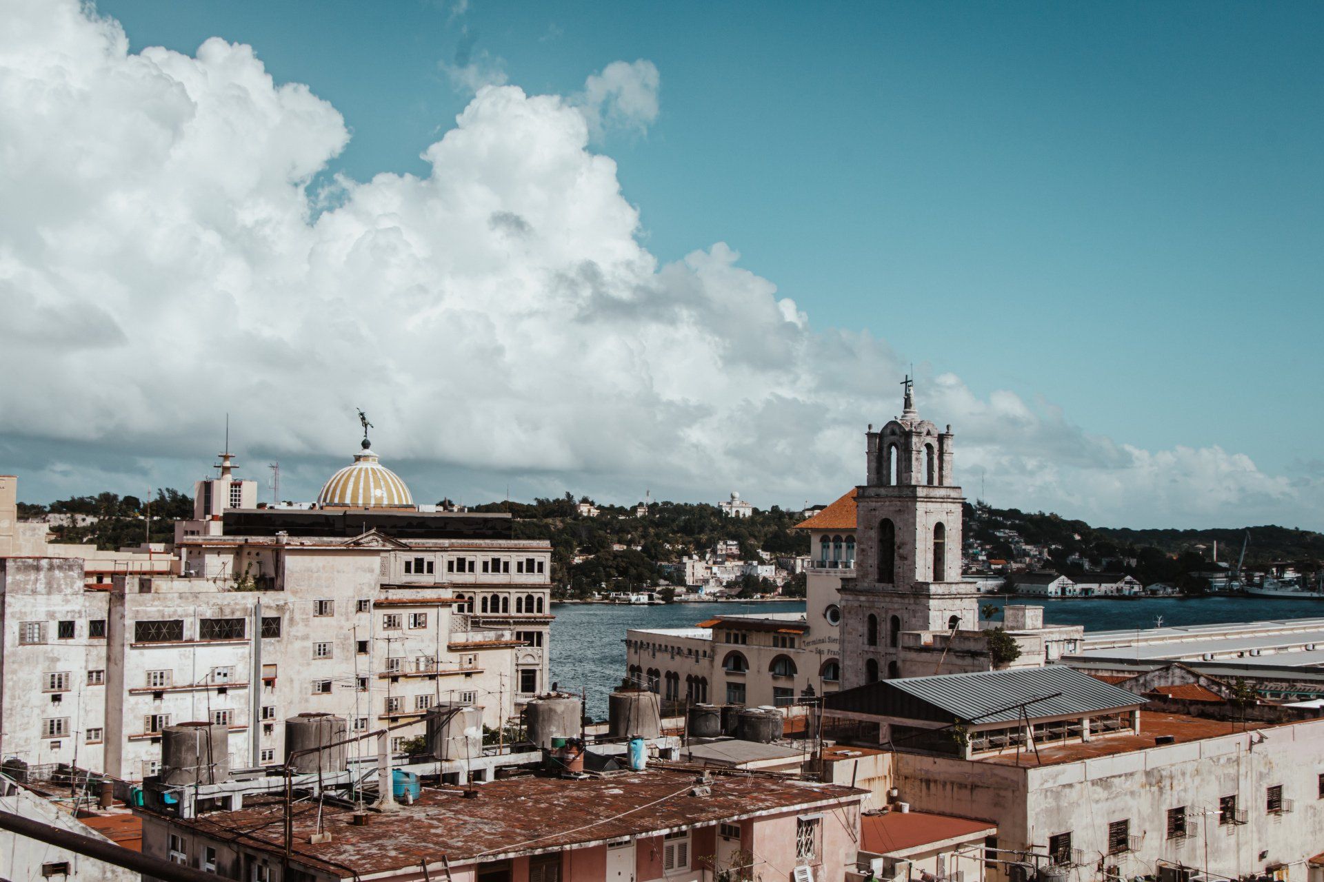 Aerial view of a Cuban city with white colonial buildings and thunderclouds in a blue sky. The city