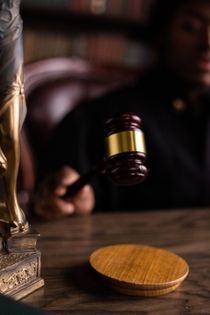 A judge is holding a gavel in front of a statue of justice.