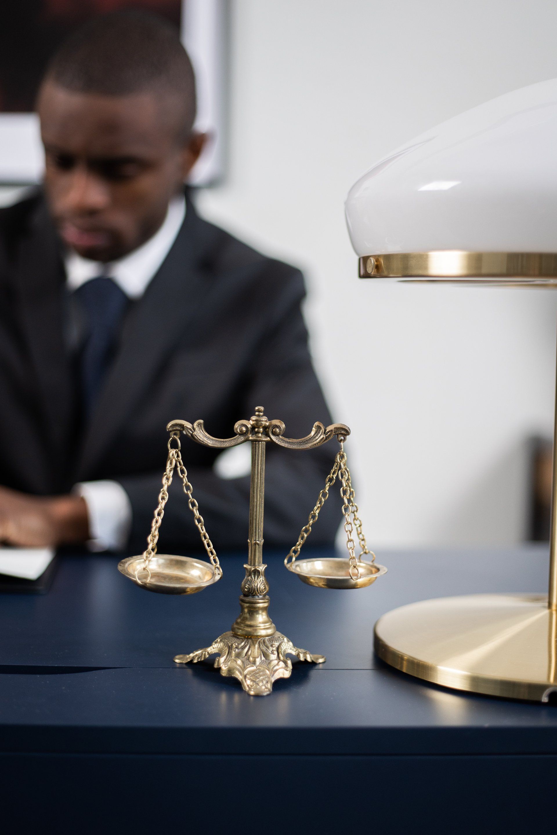 A professional black man lawyer is sitting behind a wooden table with a balanced scale in front