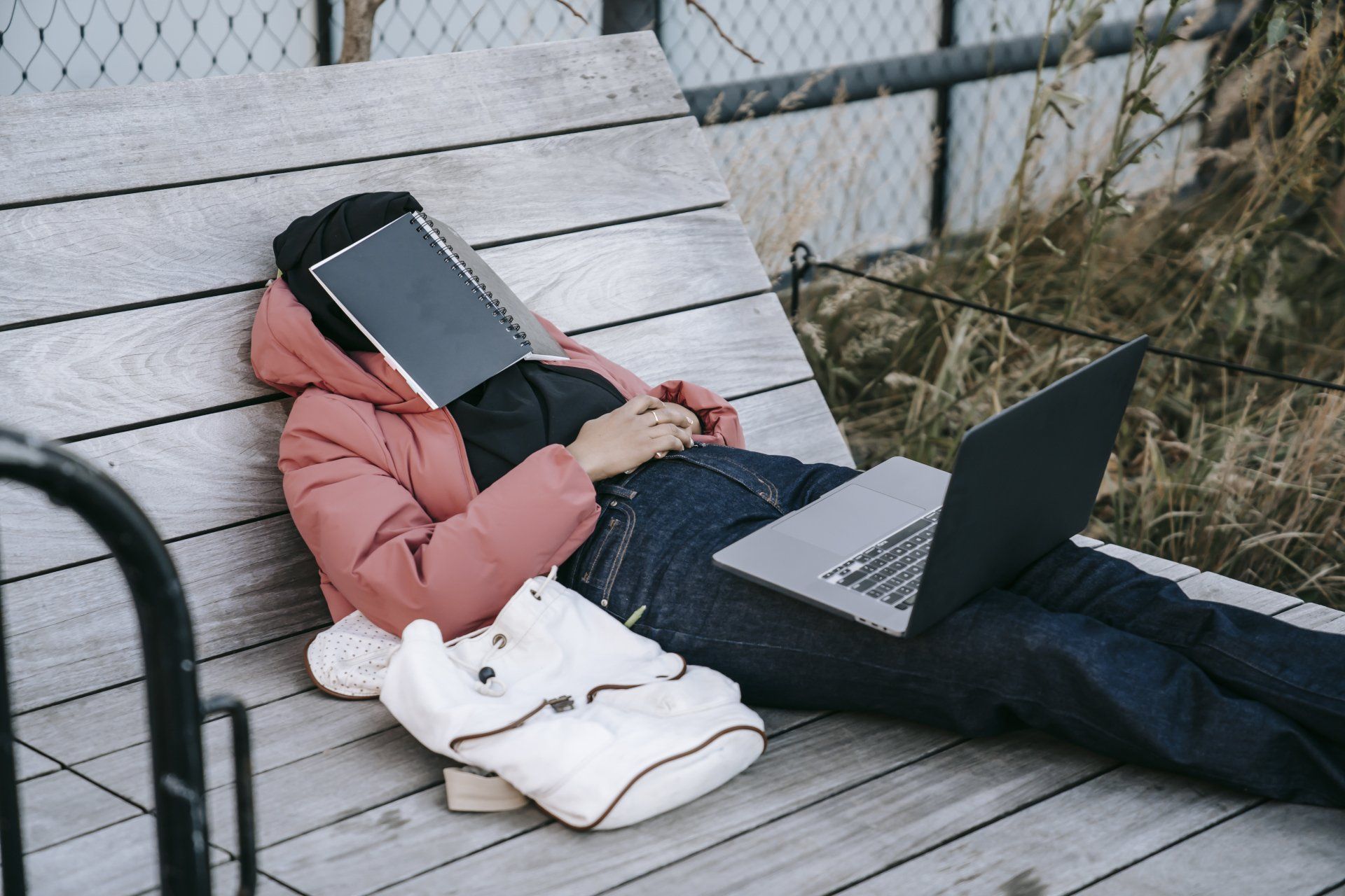 a woman laying on a bench with a laptop and a notebook on her face