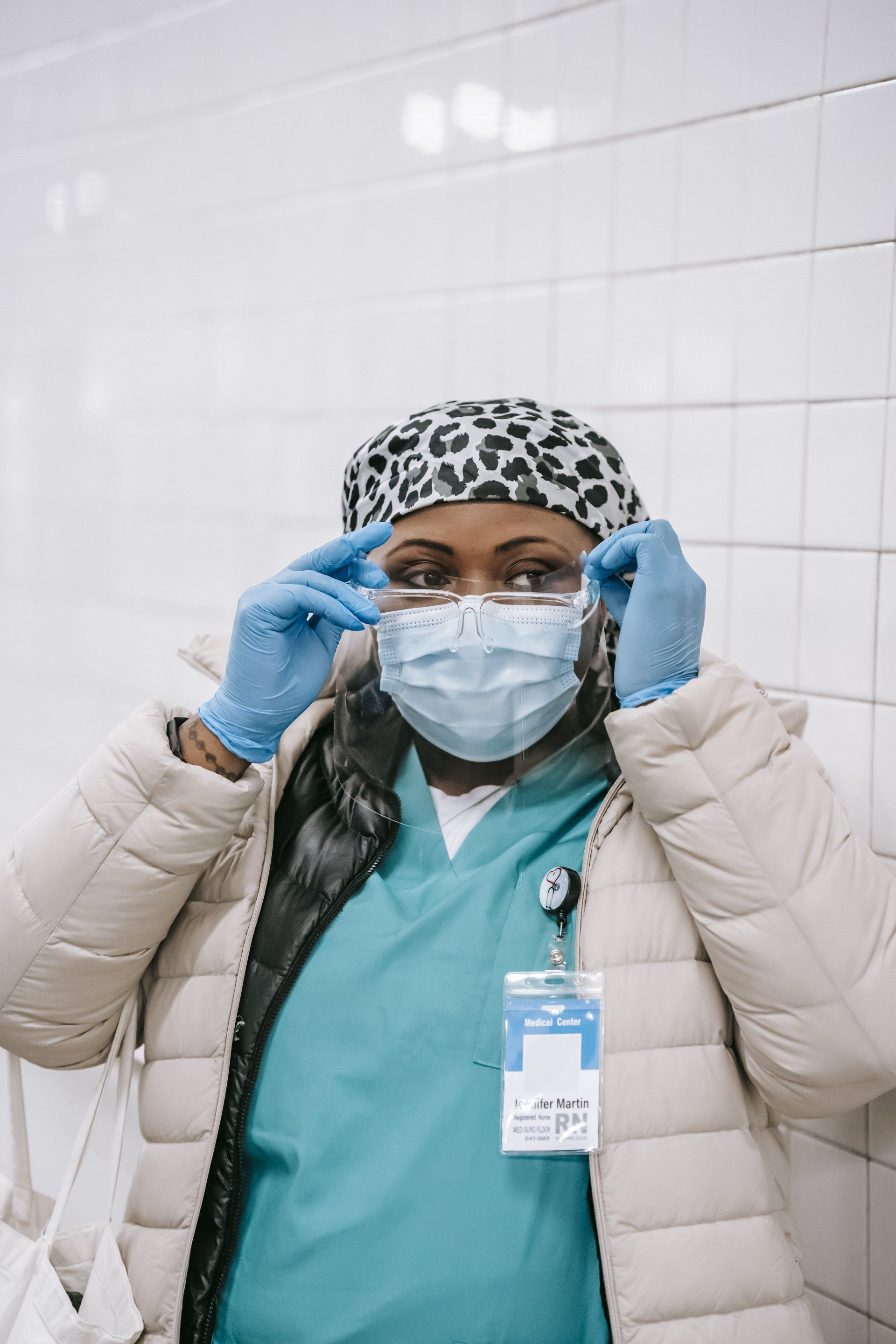 A nurse wearing a mask and gloves is putting on her glasses.
