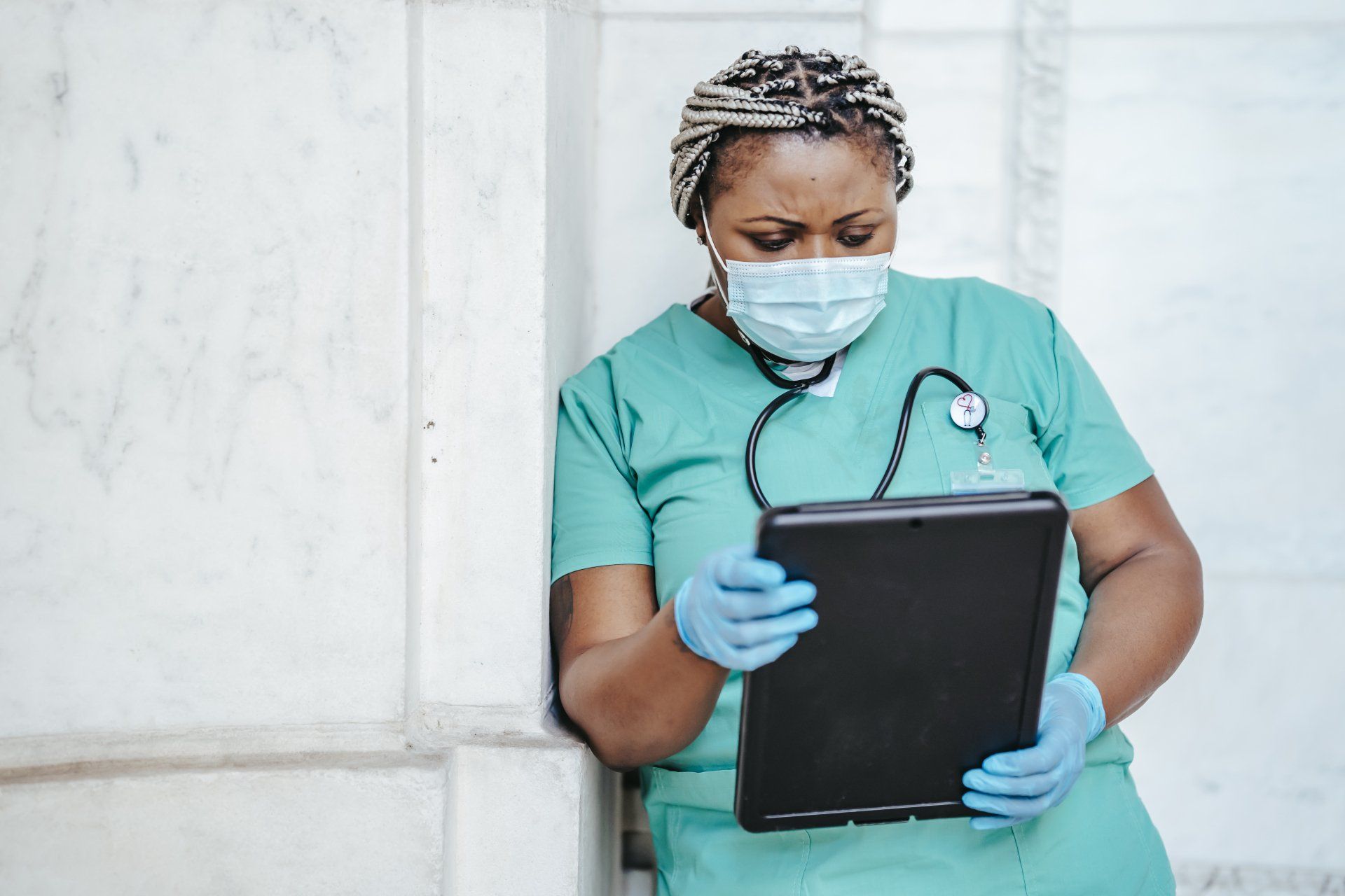 A nurse wearing a mask and gloves is using a tablet computer.