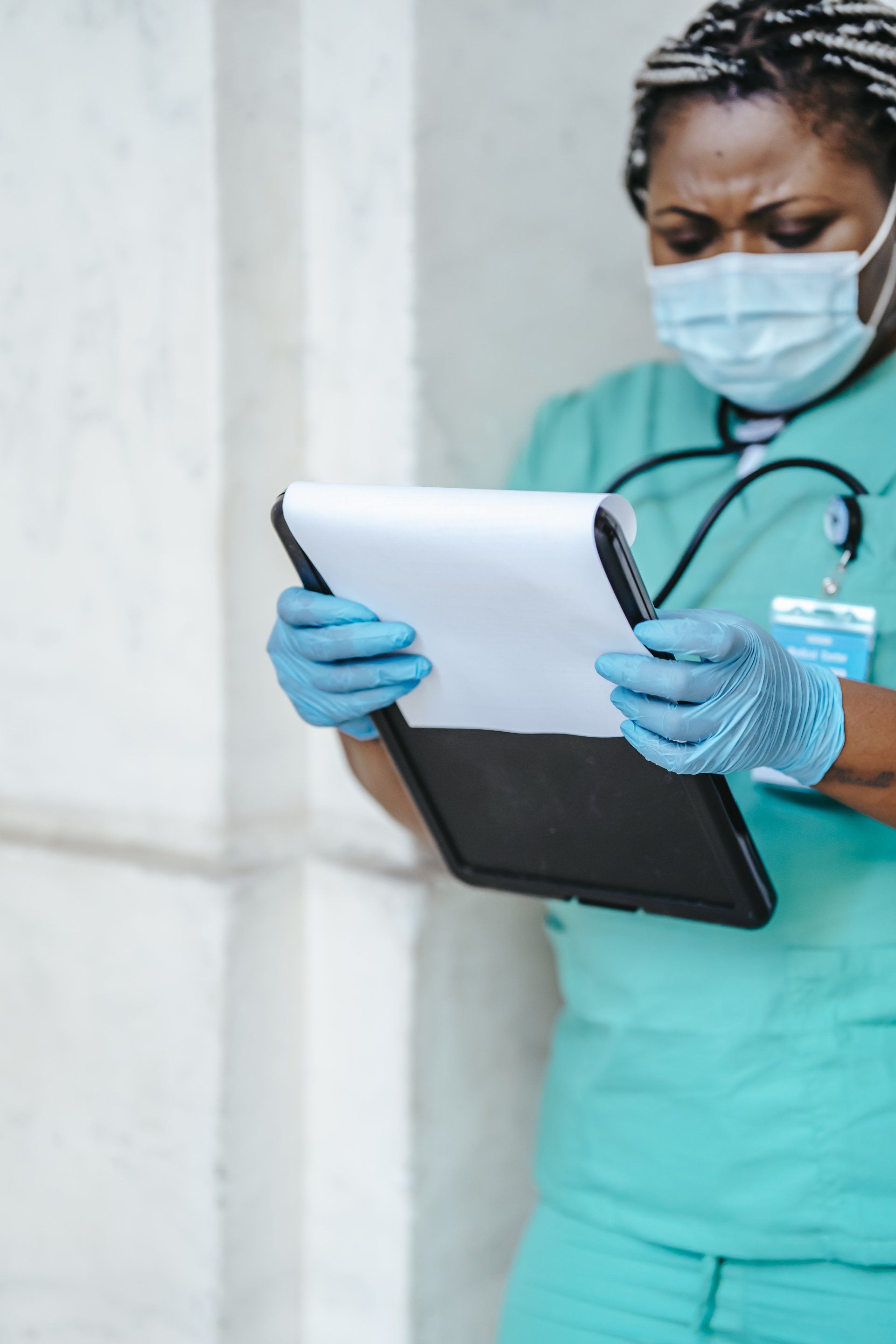 A nurse wearing a mask and gloves is looking at a tablet.