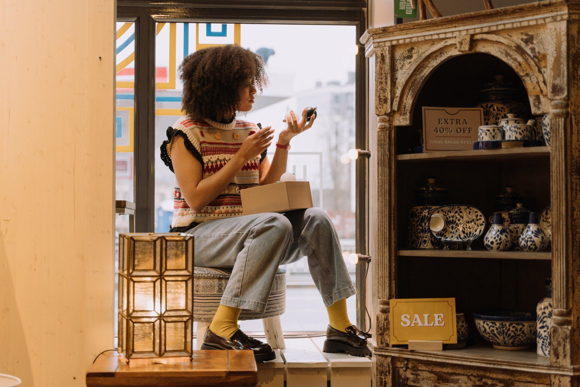 a woman is sitting on a window sill in a store holding a box .