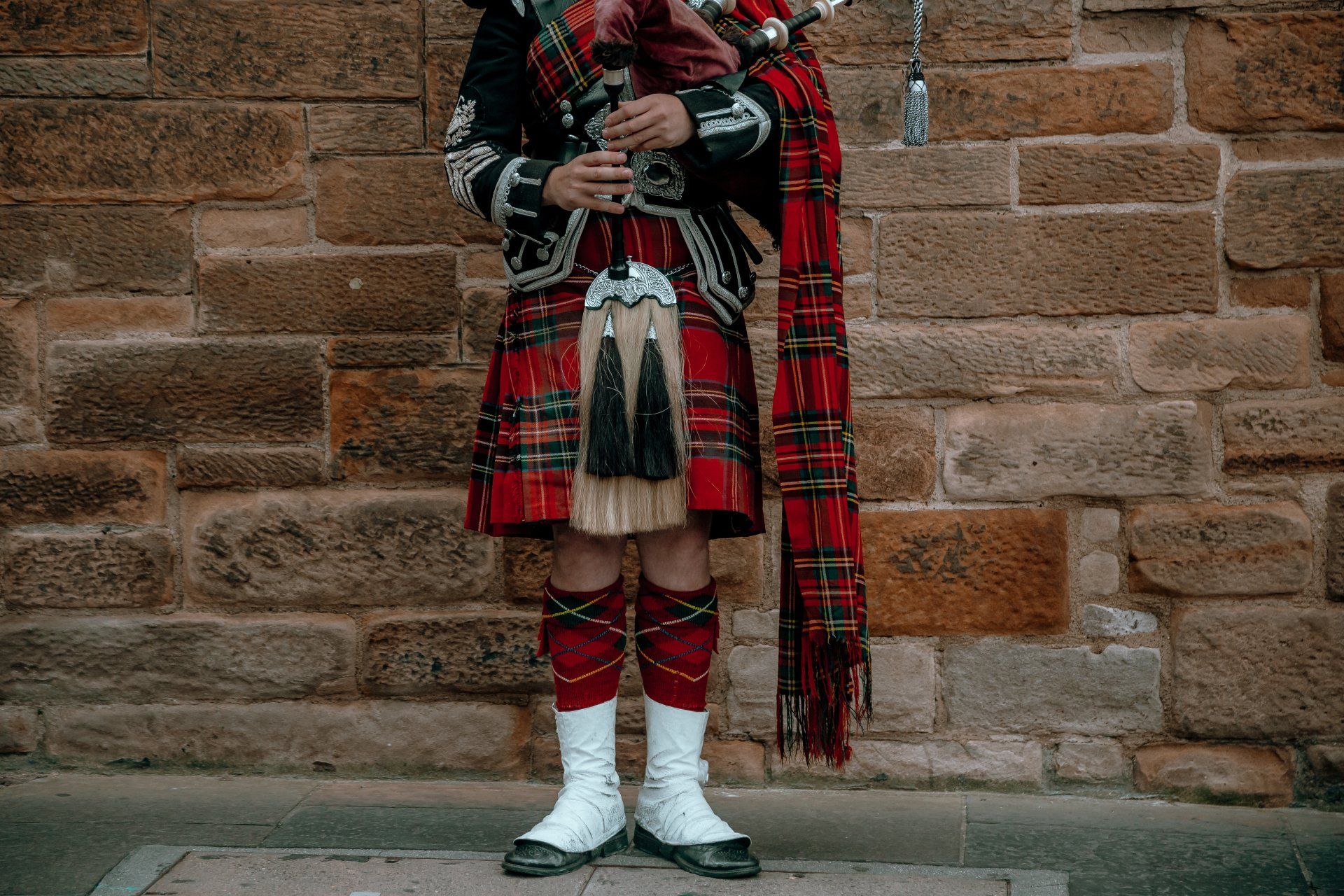 A man in a kilt is playing a bagpipe in front of a brick wall symbolic of a customer avatar in marketing.