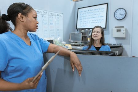 A nurse is standing at a counter in a hospital holding a tablet.