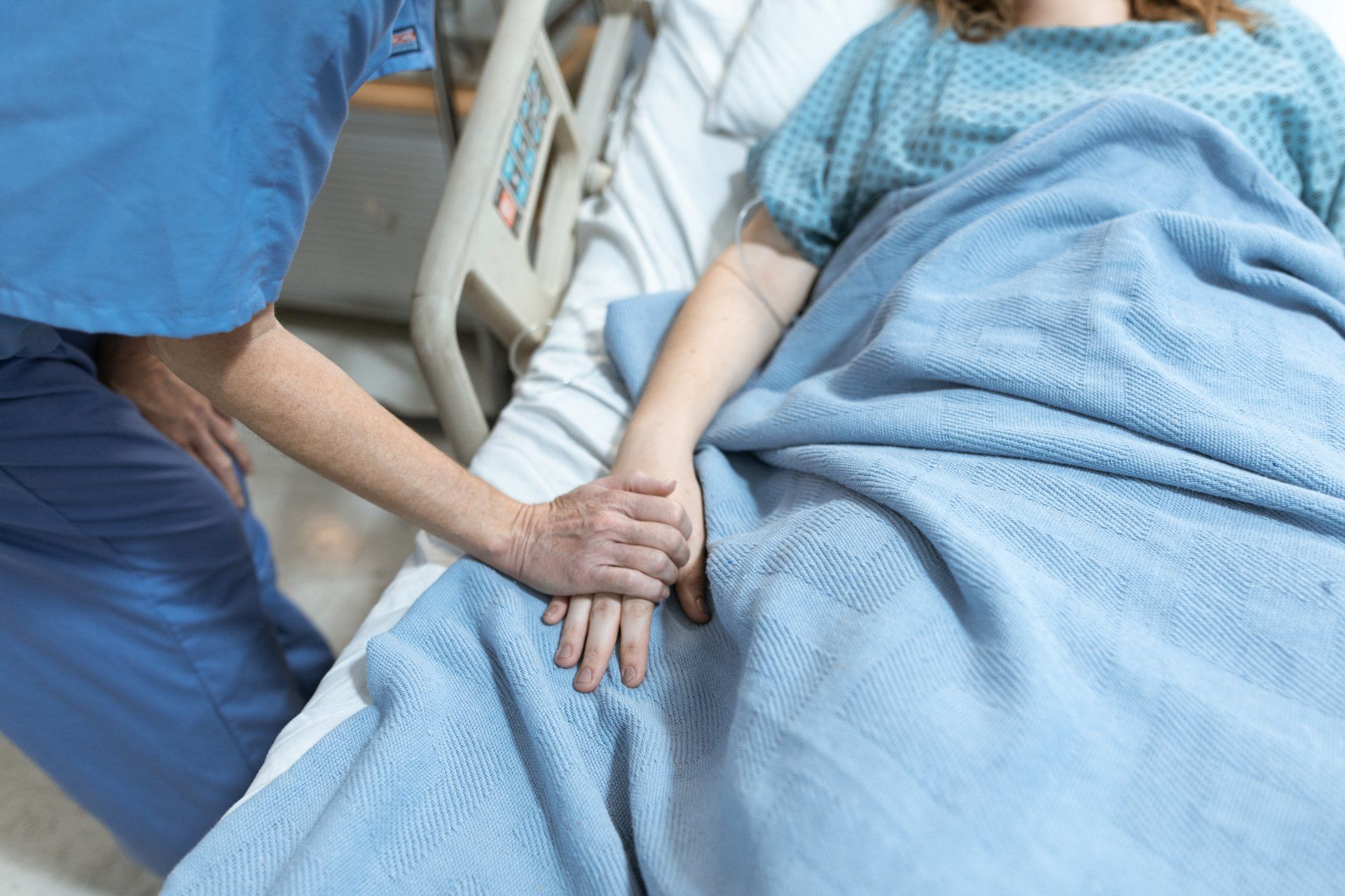 A nurse is holding the hand of a patient in a hospital bed.