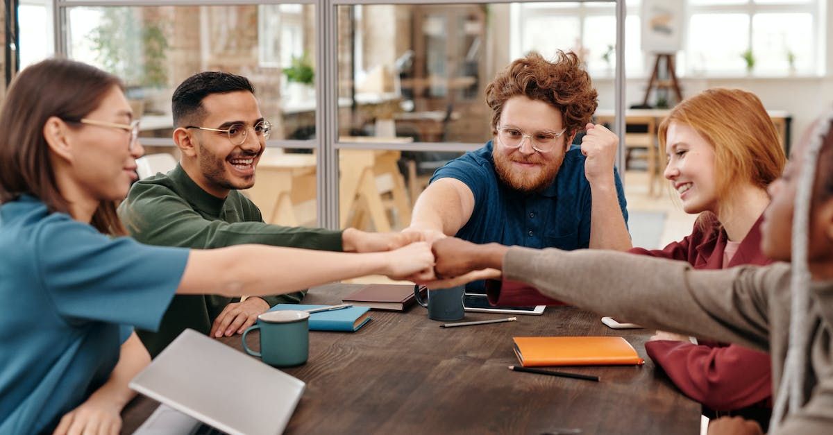 a group of people are sitting around a table putting their hands together .