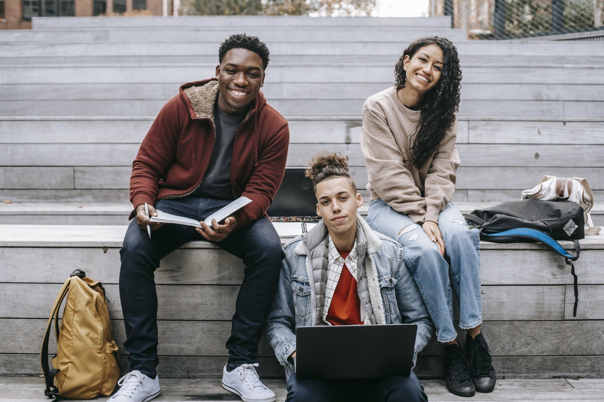 A group of young people are sitting on a set of stairs with a laptop.