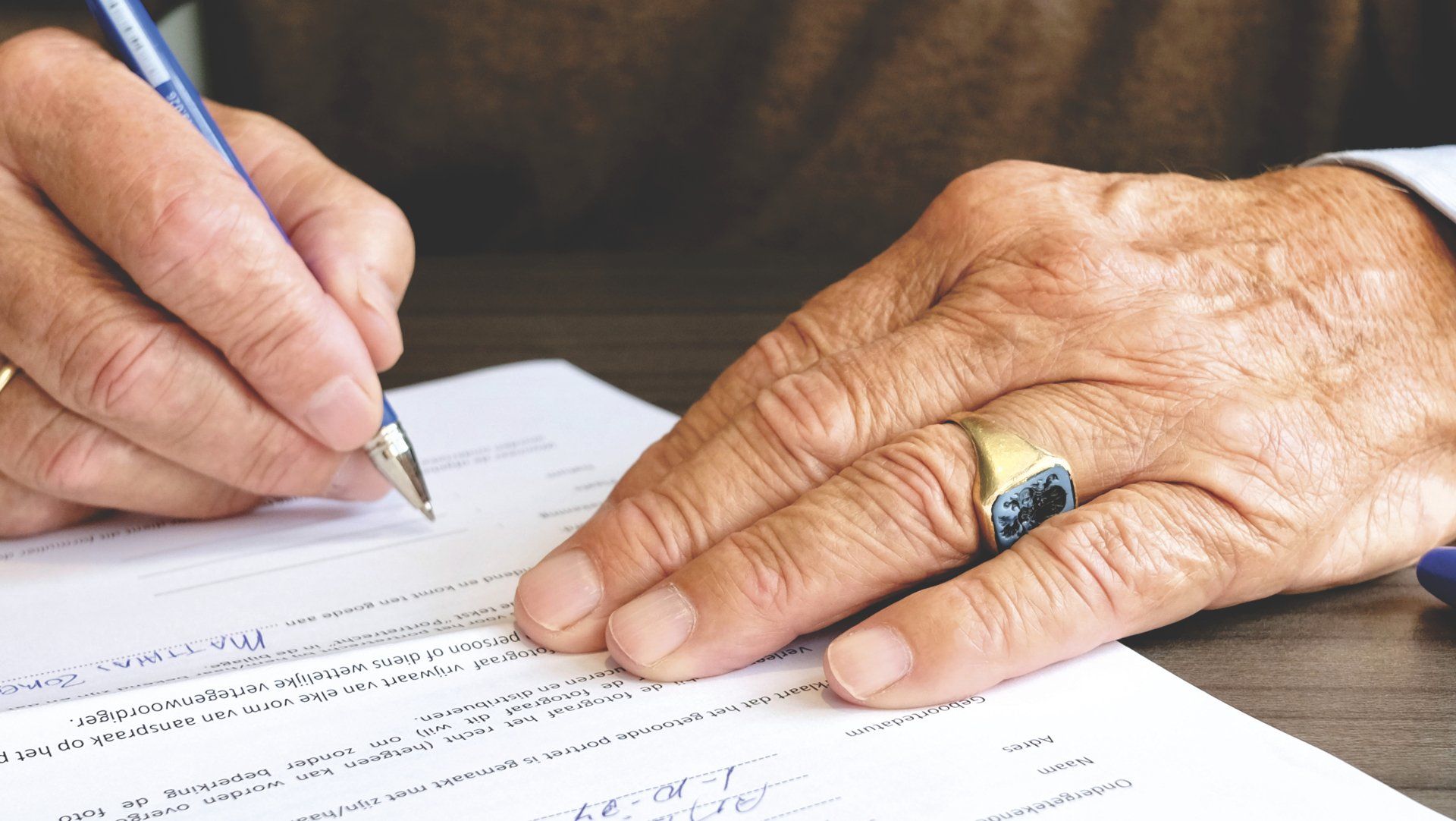 A man with a ring on his finger is writing on a piece of paper.