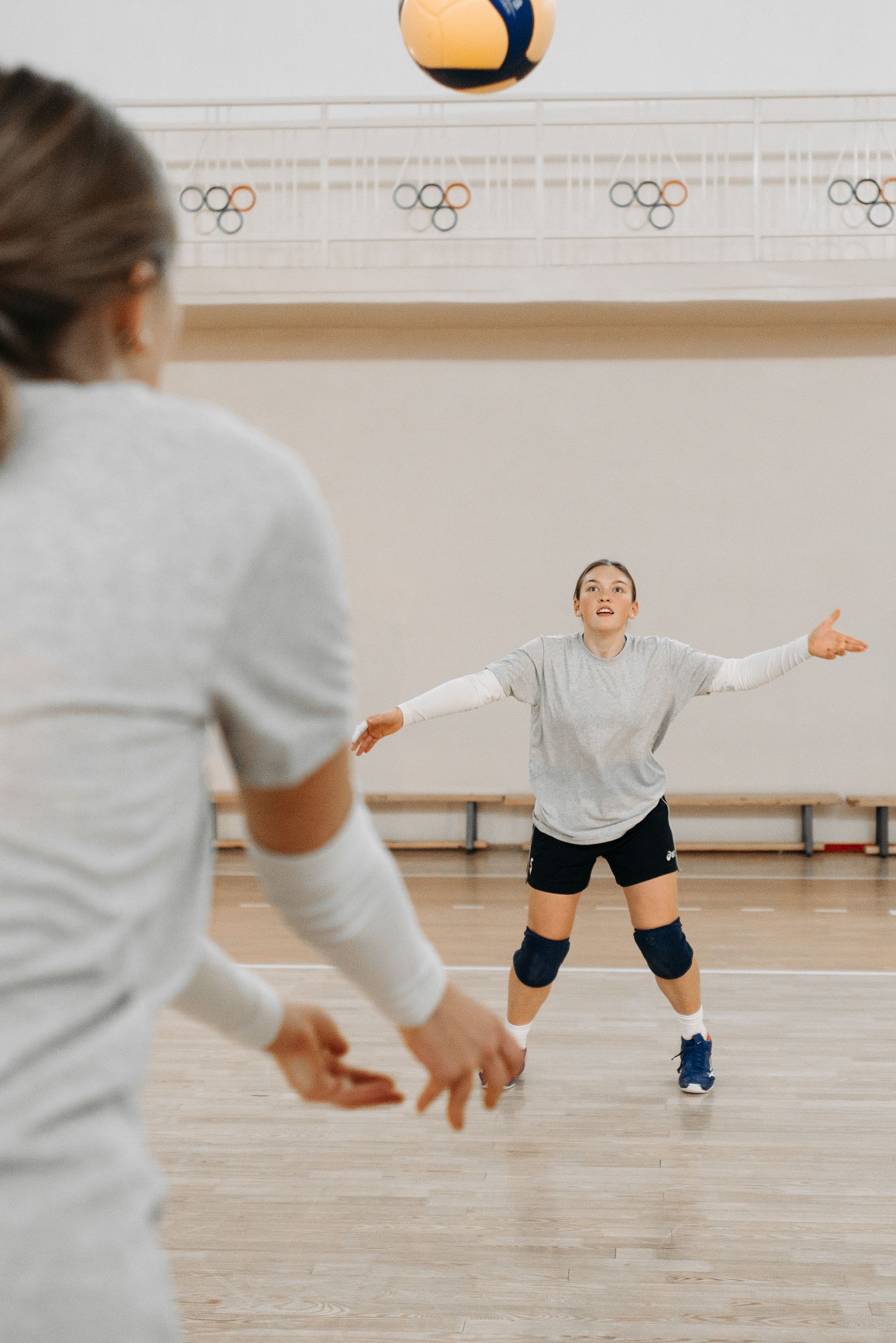 Two women are playing volleyball in a gym.