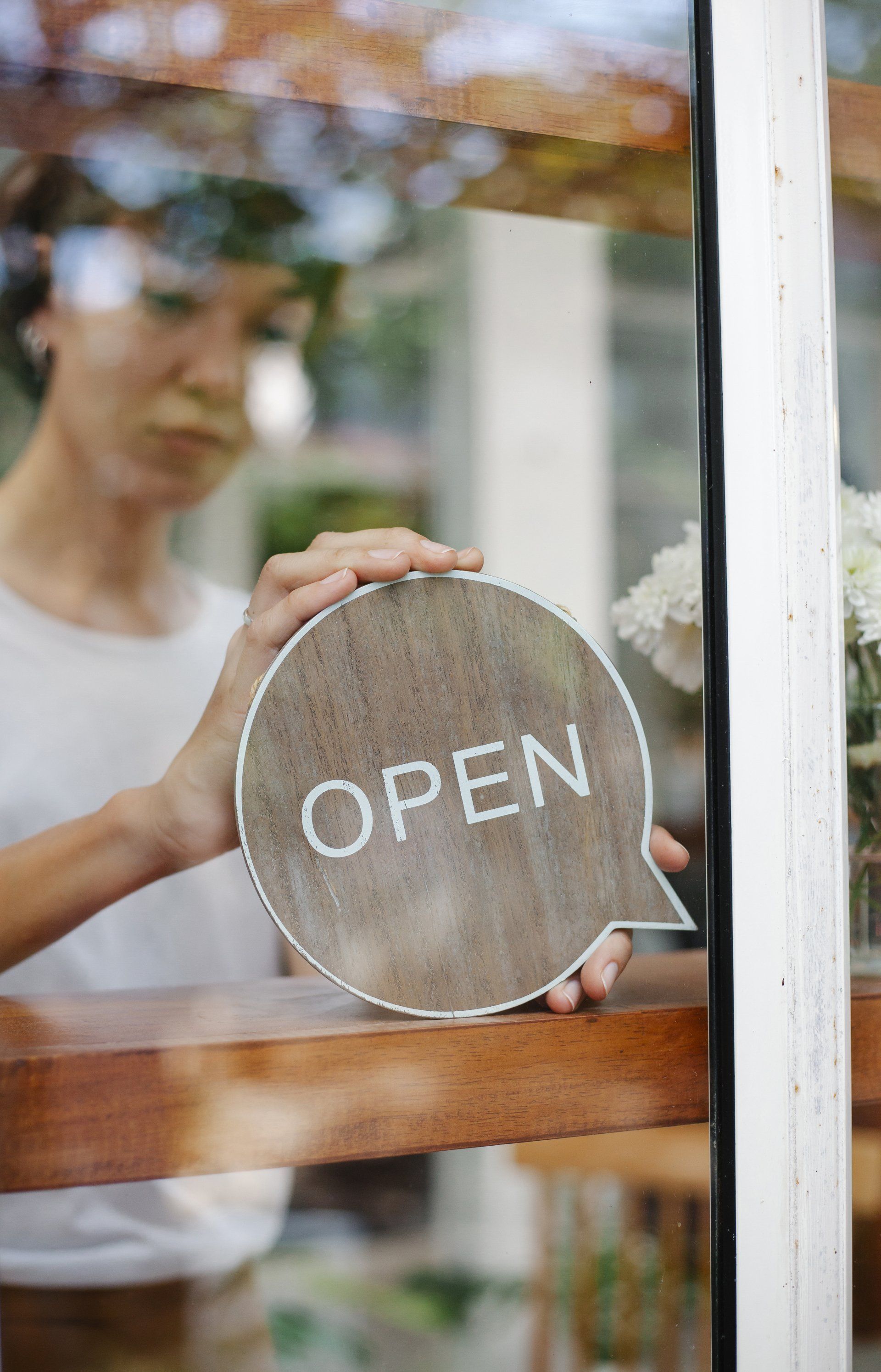 A woman is holding an open sign in front of a glass door.