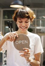 A woman is holding a wooden sign that says open.