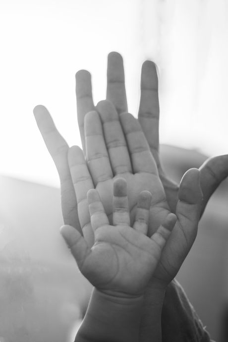 A black and white photo of a person holding a baby 's hands.