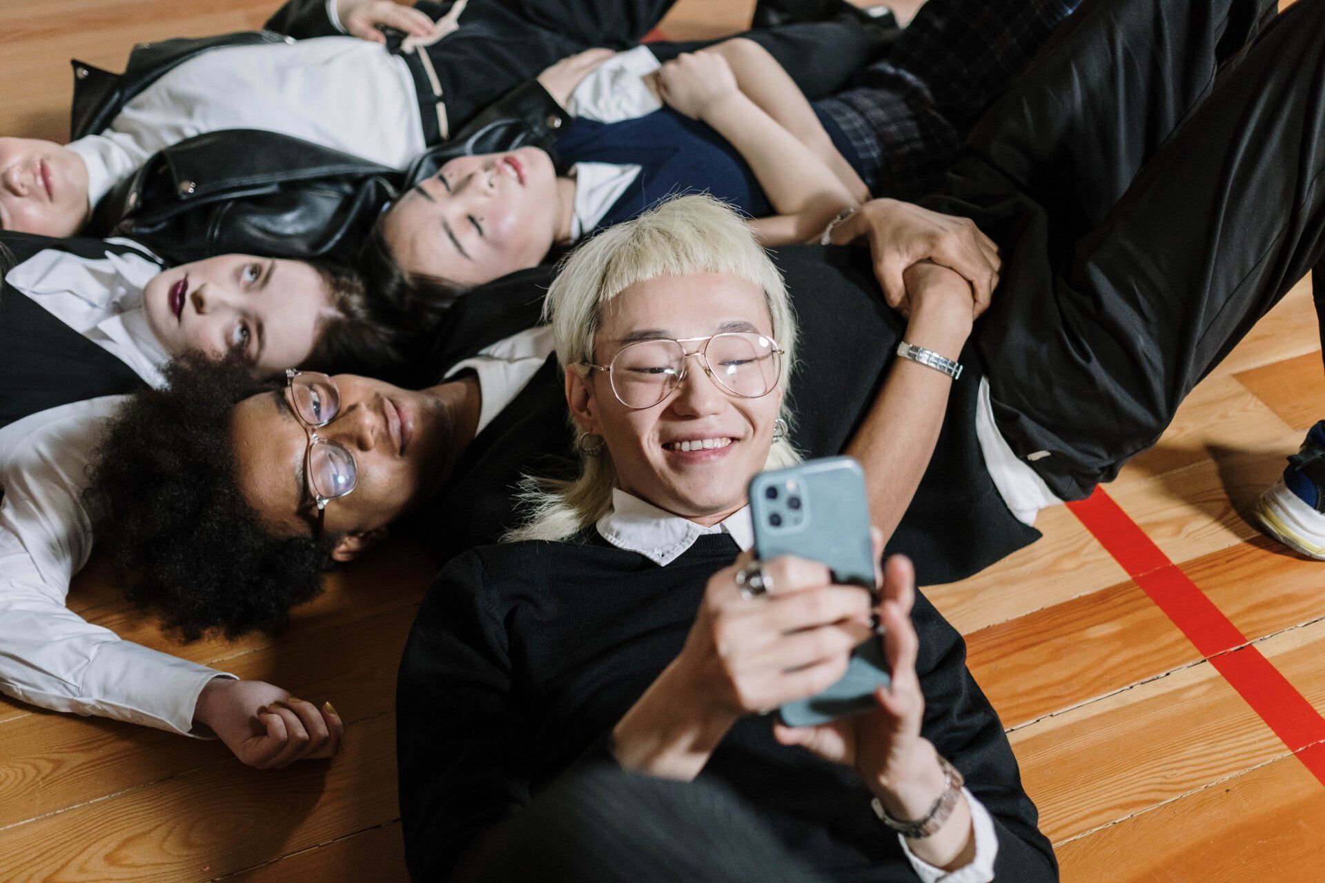 A group of people are laying on the floor looking at a cell phone.