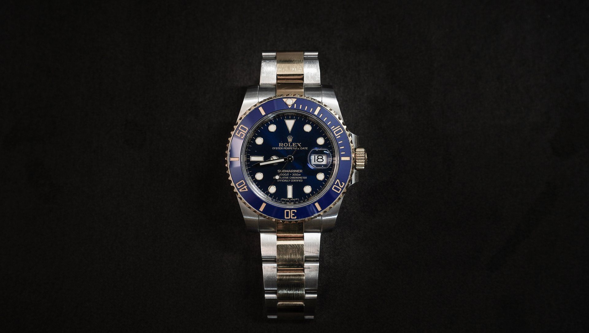 A silver and blue rolex watch is sitting on a black surface.