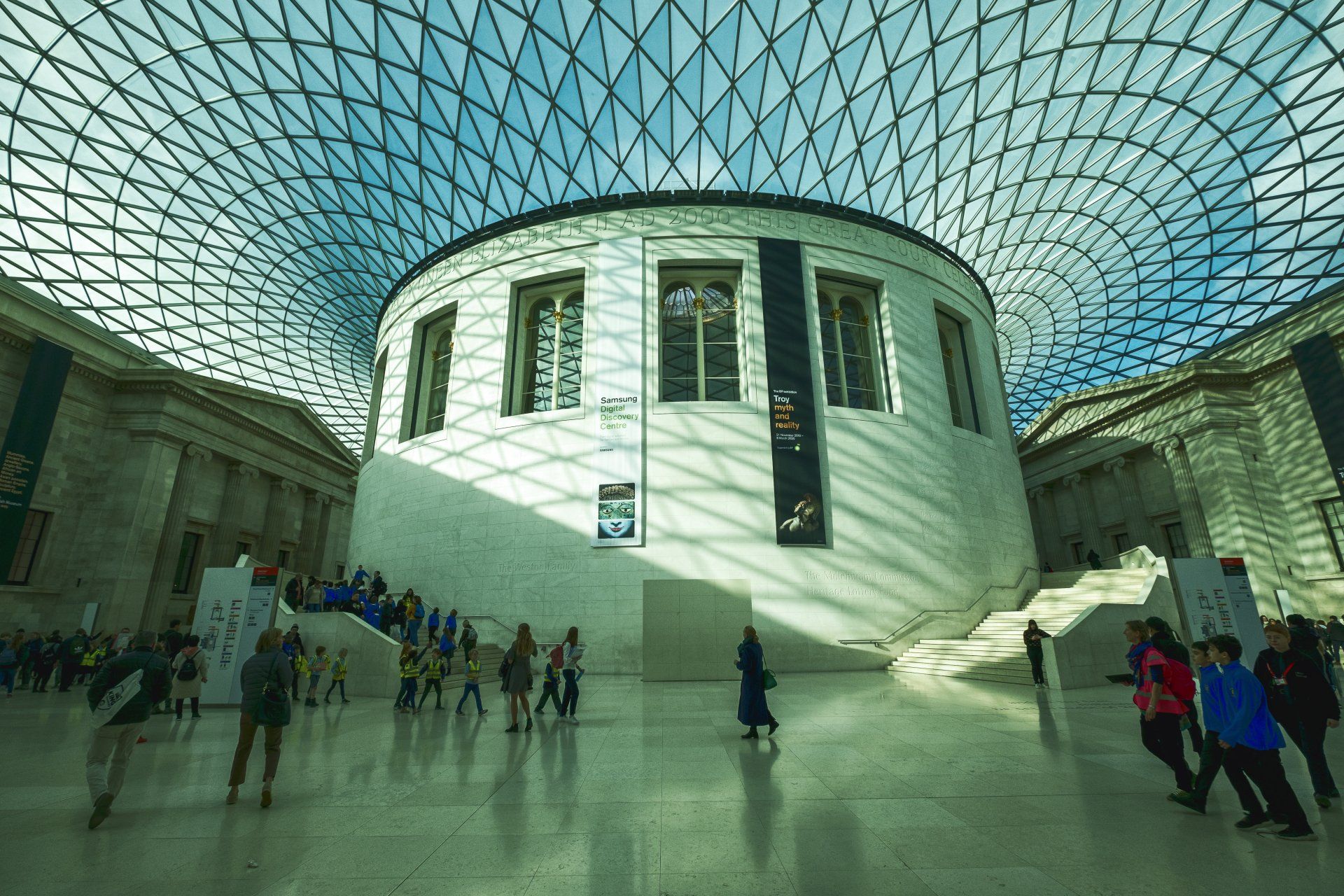 A group of people are standing in front of a large building with a glass ceiling.