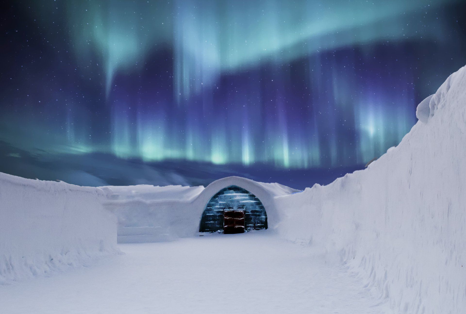 The aurora borealis is visible over an igloo in the snow.