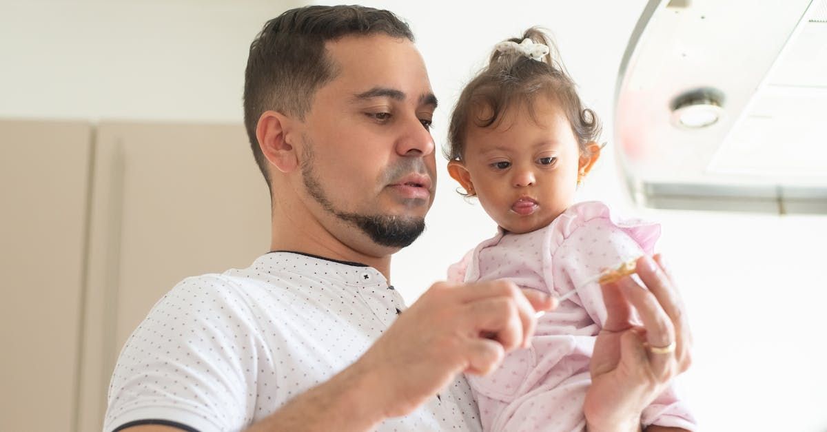 Man holding baby in a kitchen, offering food. Both looking at food.