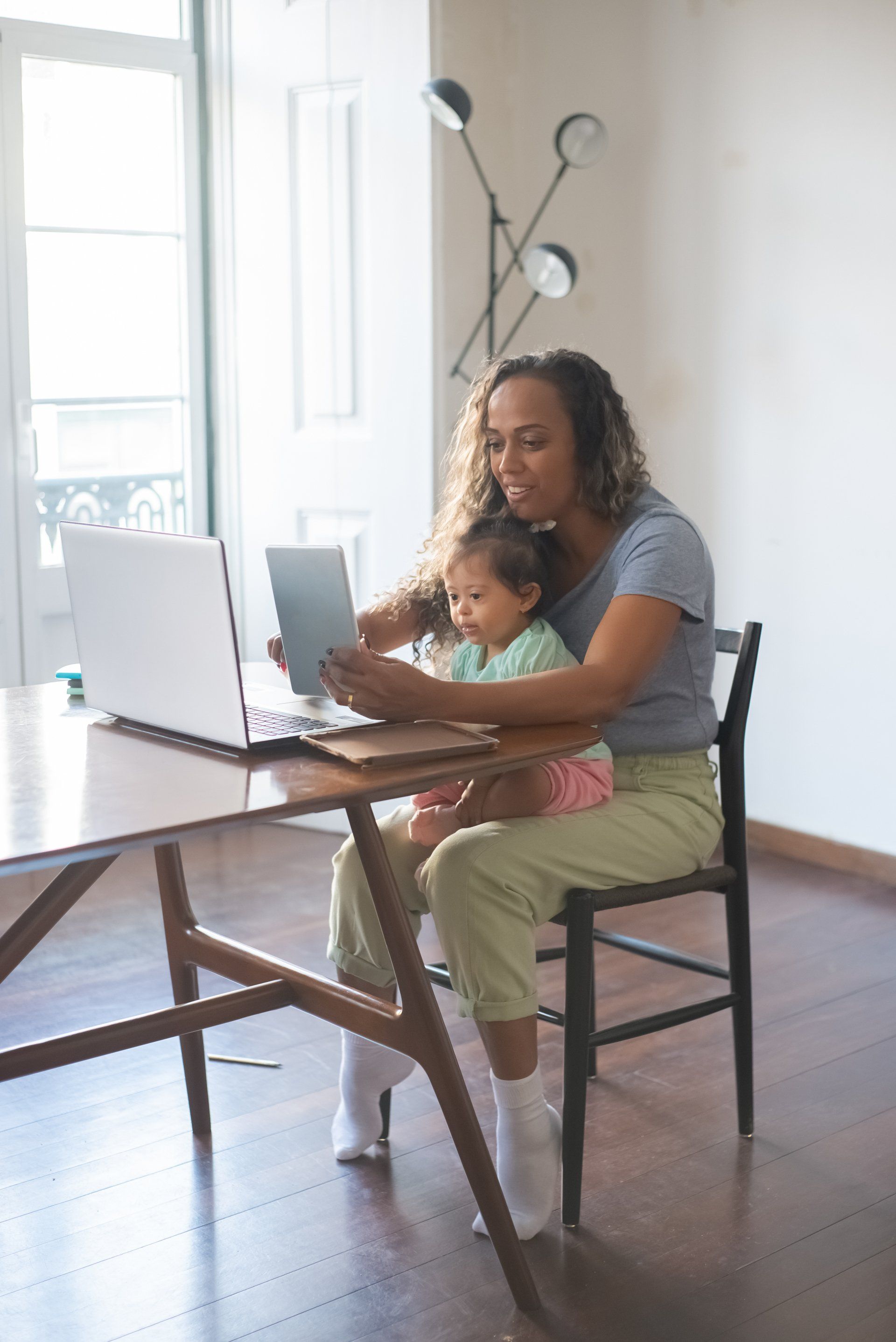 A woman is holding a child while using a laptop computer.