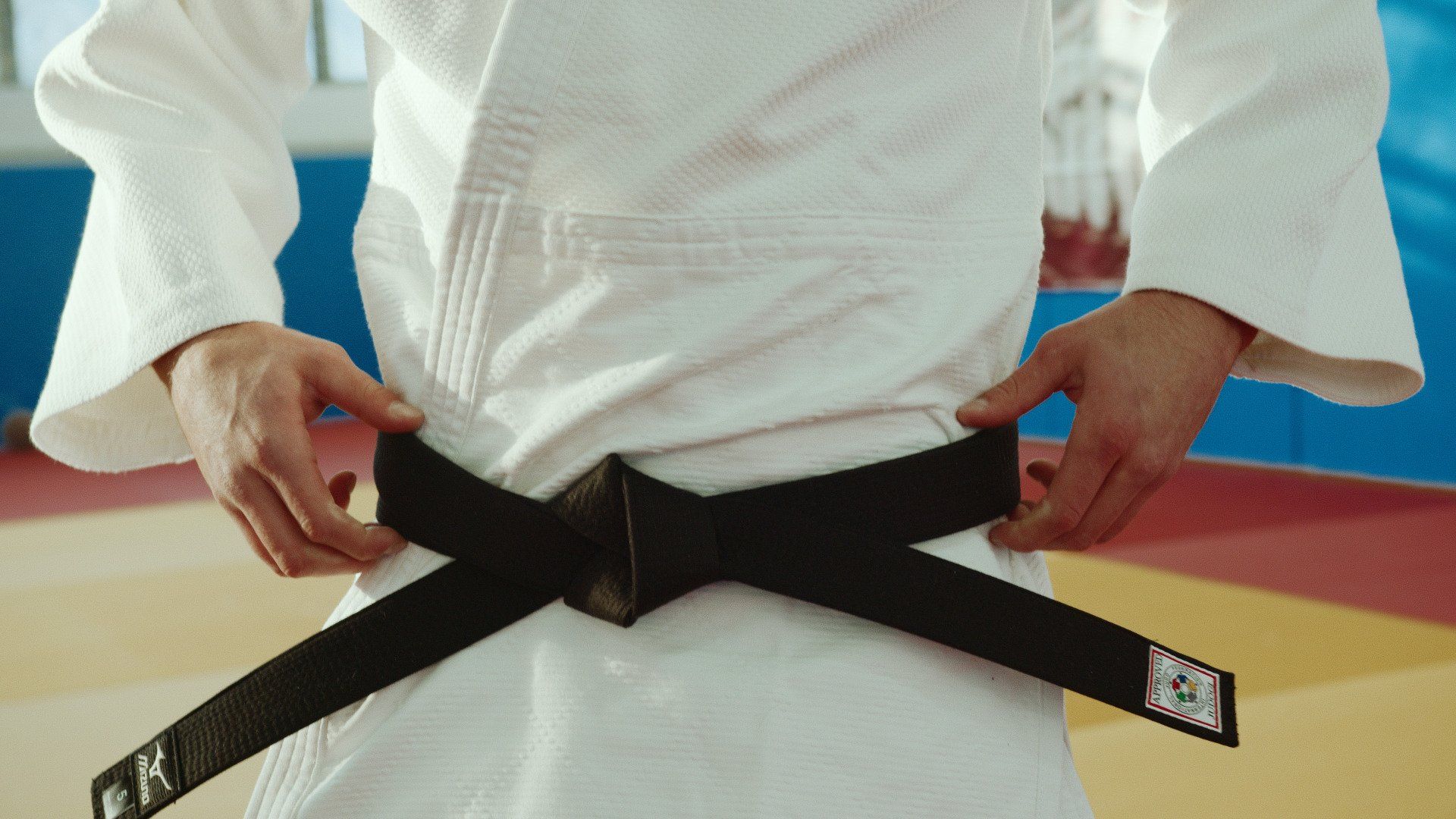 Een persoon in een wit karate-uniform bindt een zwarte band om zijn middel.