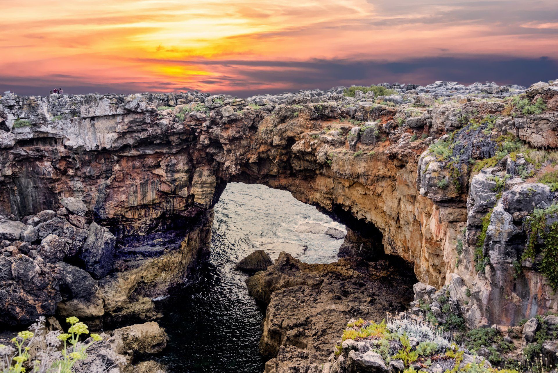 a sunset over a rocky cliff with a cave in the middle of it .