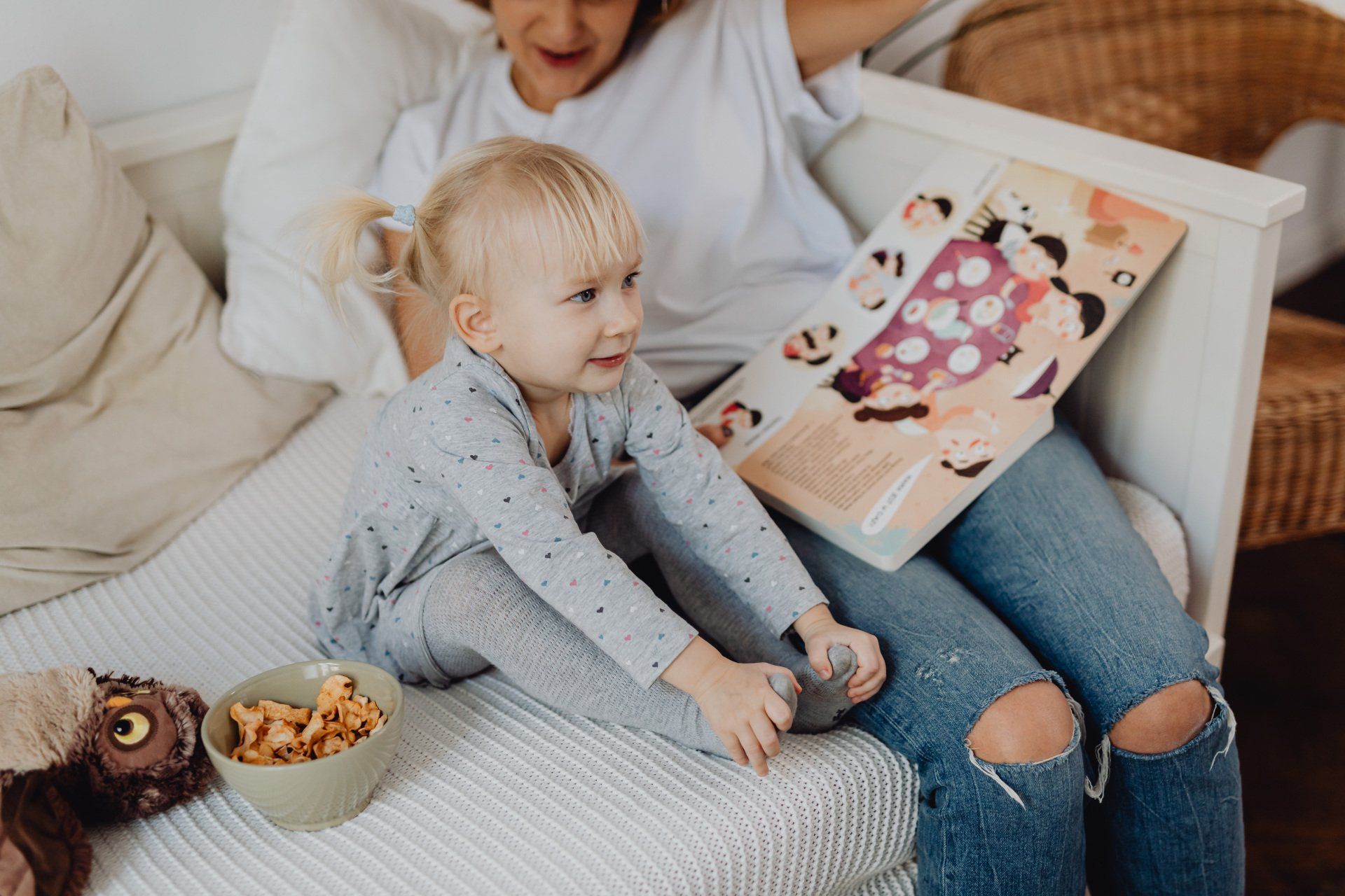 A woman is sitting on a couch reading a book to a little girl.