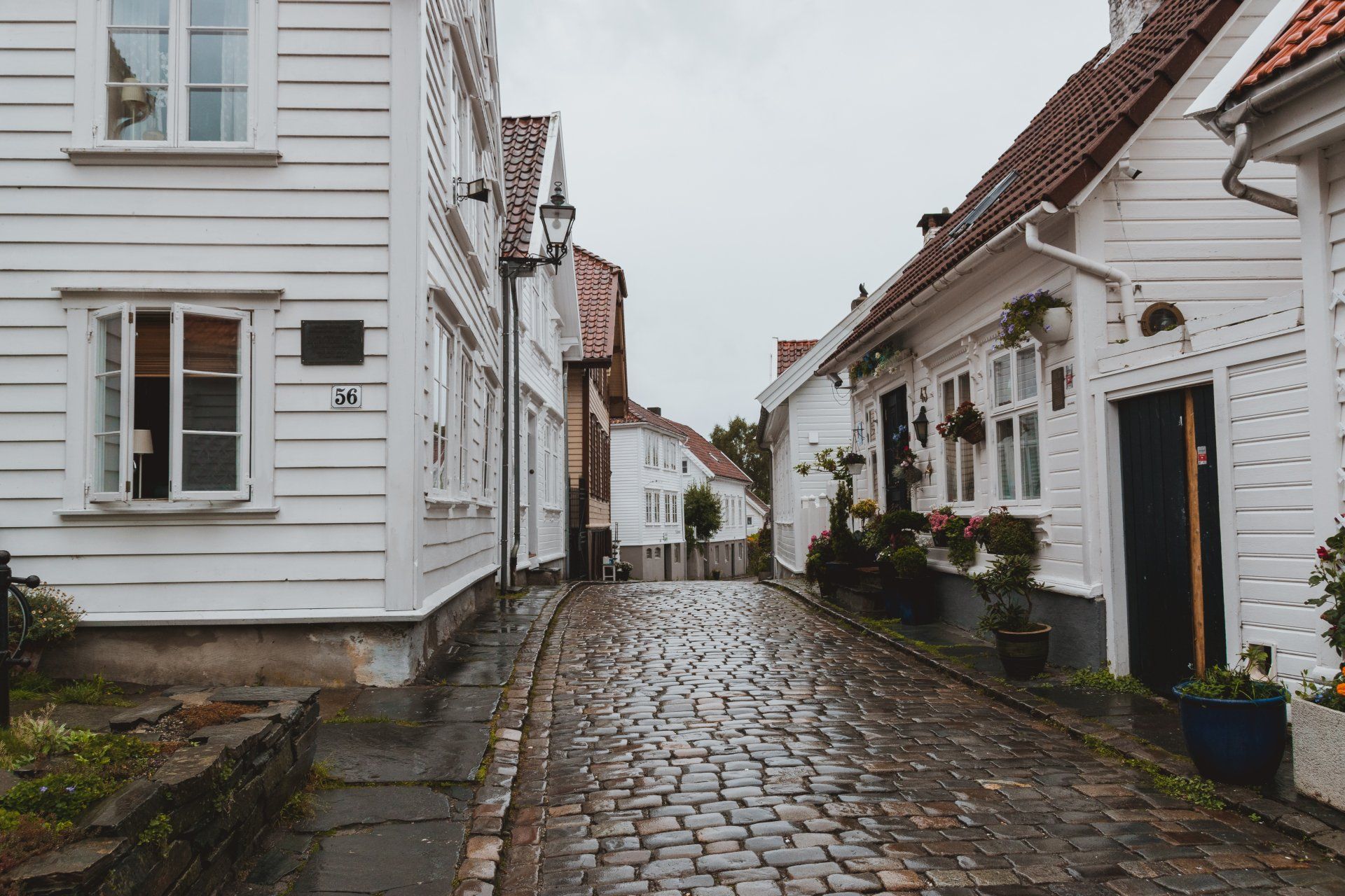 A cobblestone street between two white houses on a cloudy day.