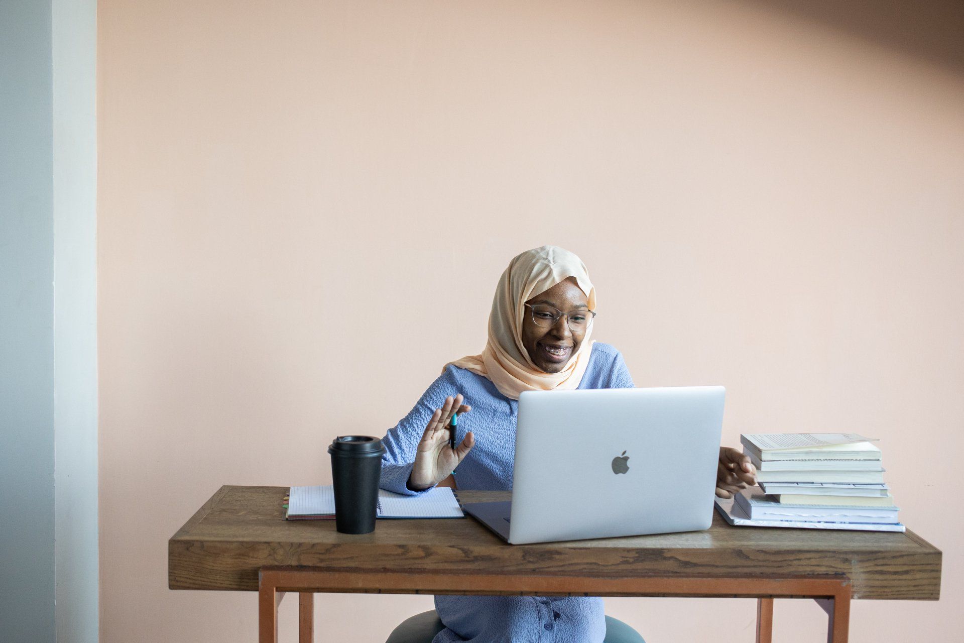 A woman in a hijab is sitting at a desk using a laptop computer.